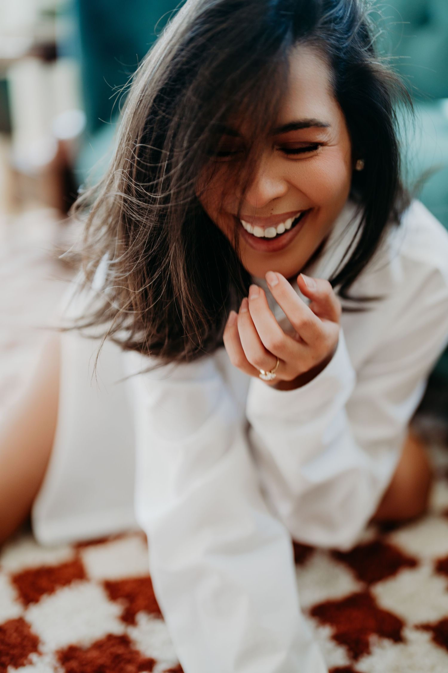 A candid portrait shows a joyful laugh while wearing a white sweater against a patterned background.