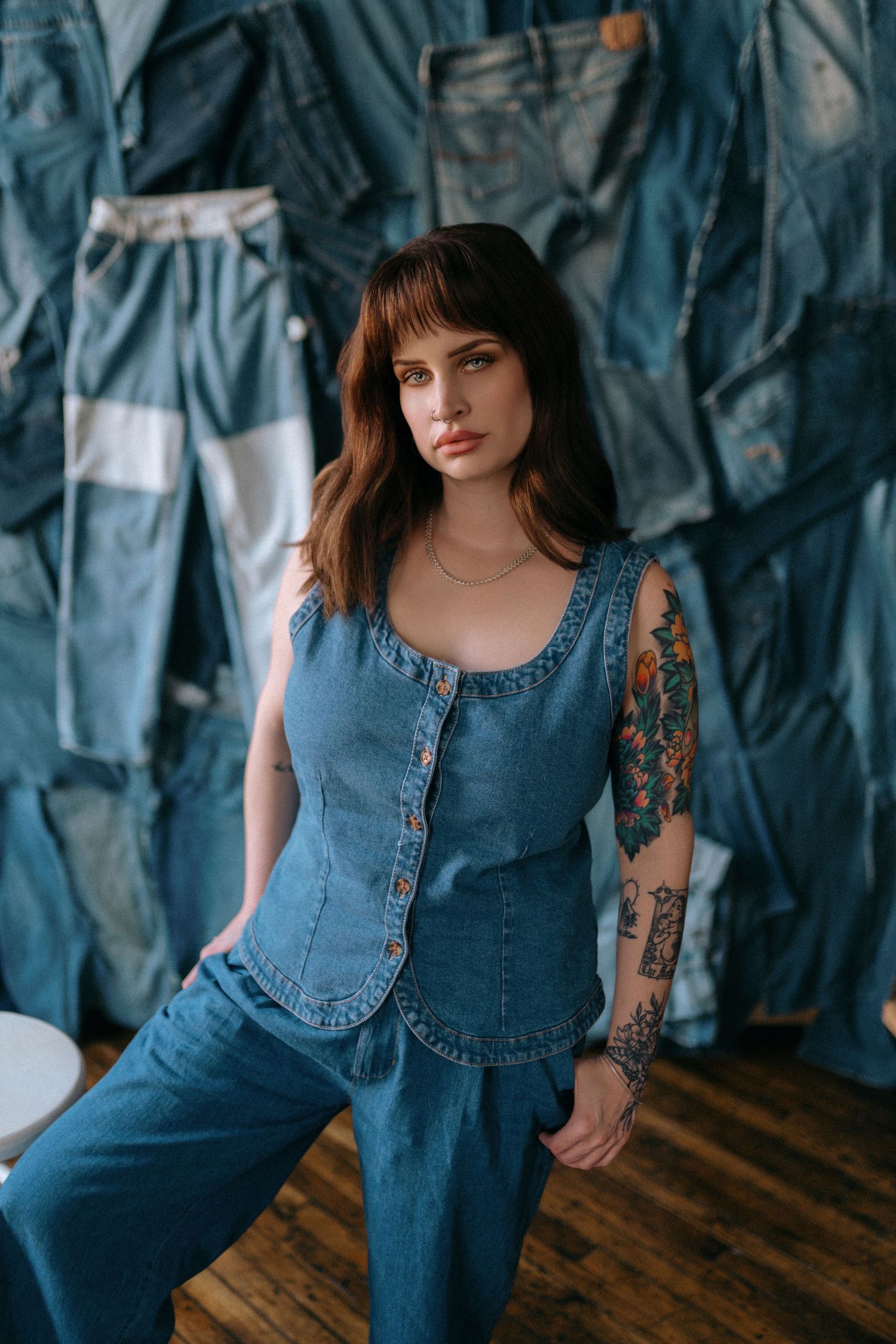 A person wearing a denim jumpsuit poses against a blue backdrop on a wooden floor.