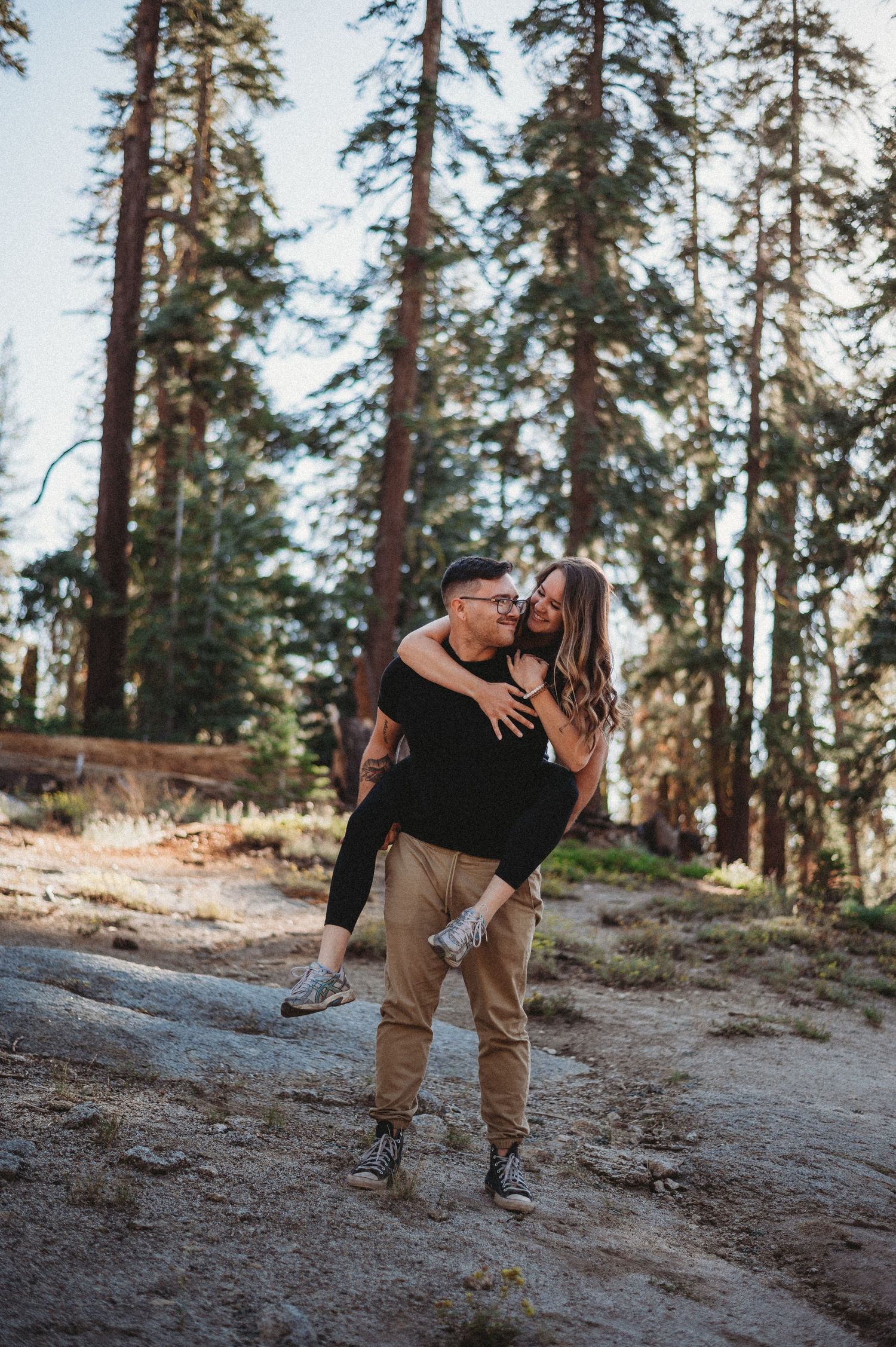 A couple shares intimate moments among tall pine trees in a mountain setting during golden hour.