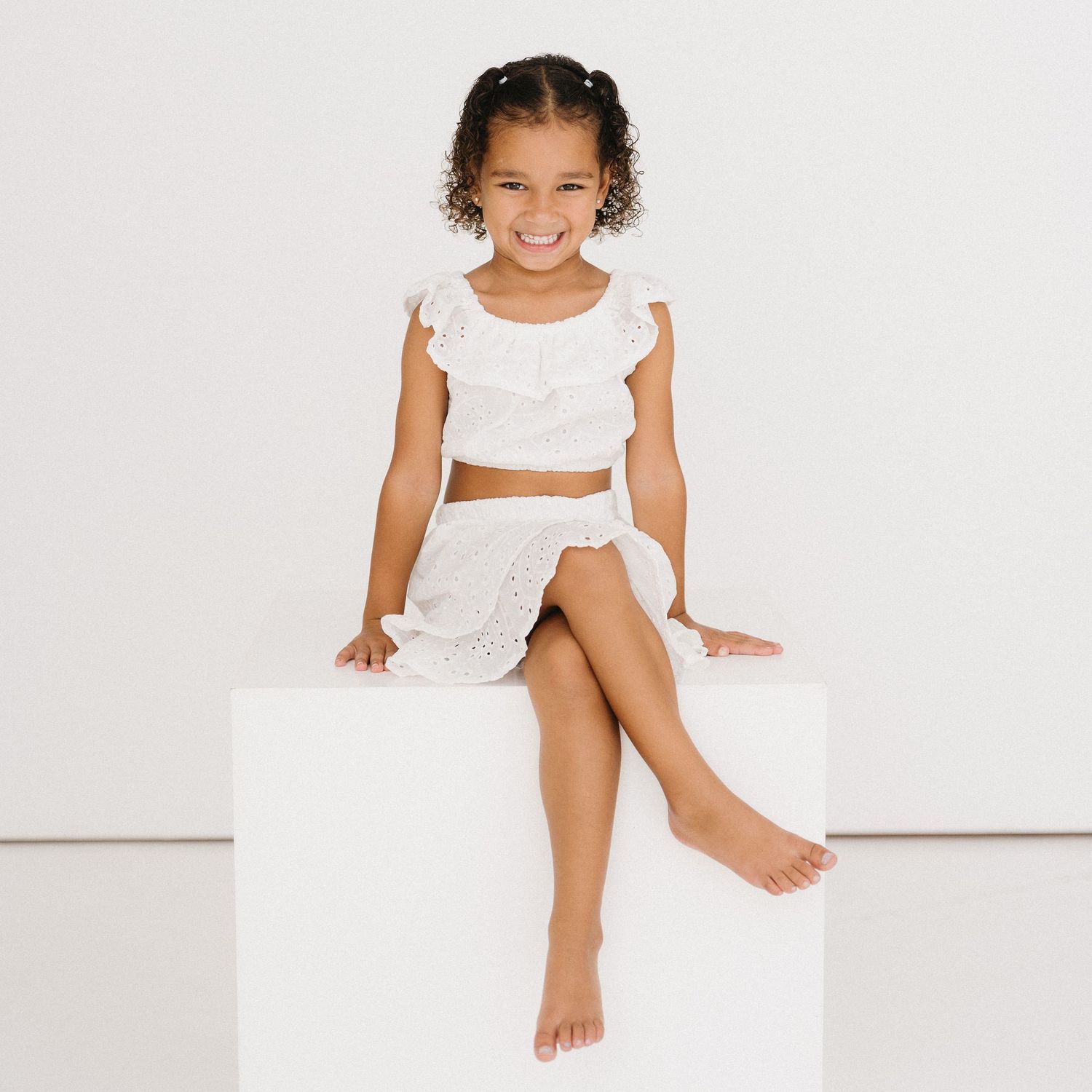 Child in white lace dress sitting and smiling on white background with playful poses.