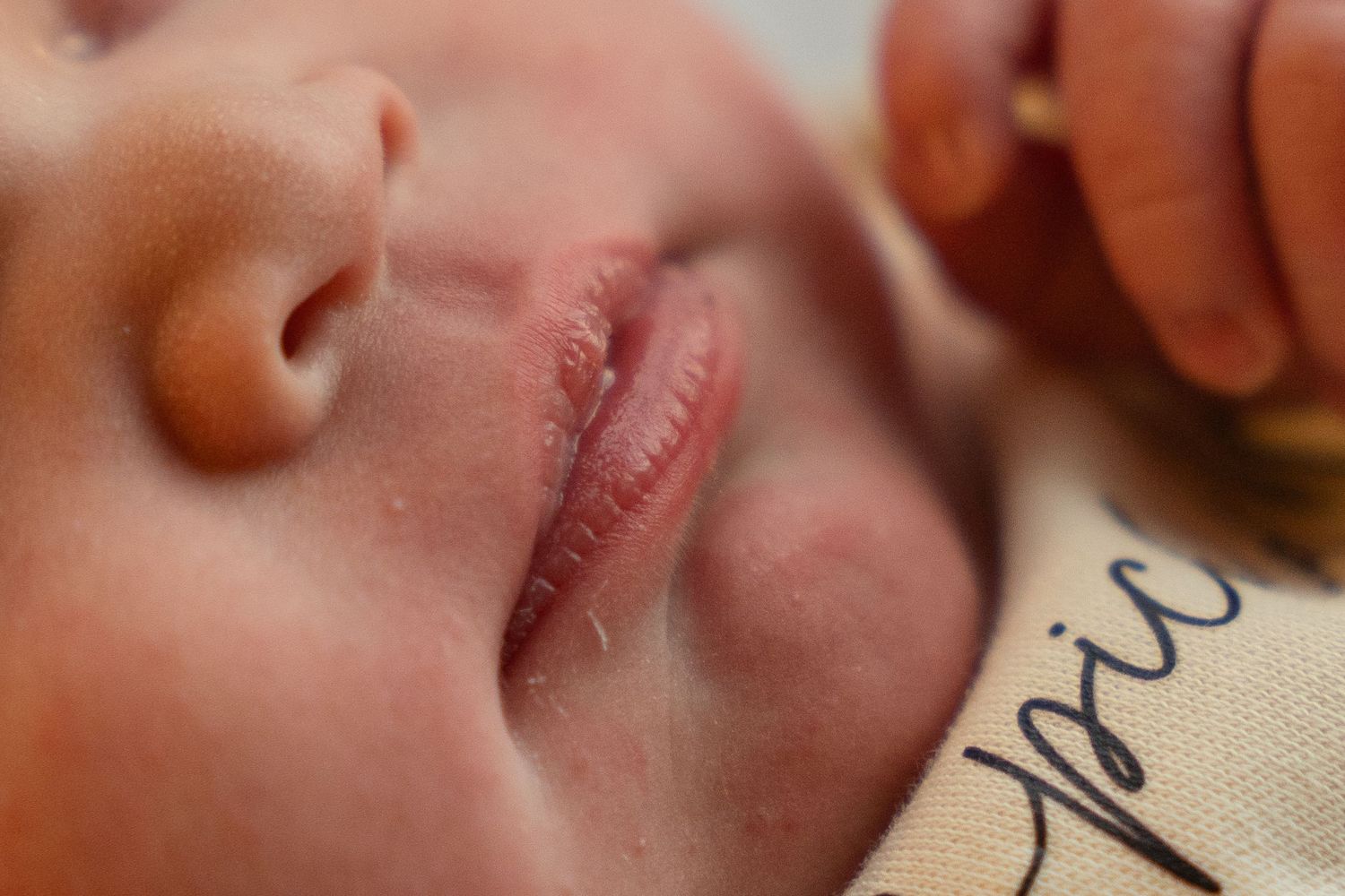 Close-up macro photograph showing a tiny baby's sleeping mouth and nose against a light beige fabric.