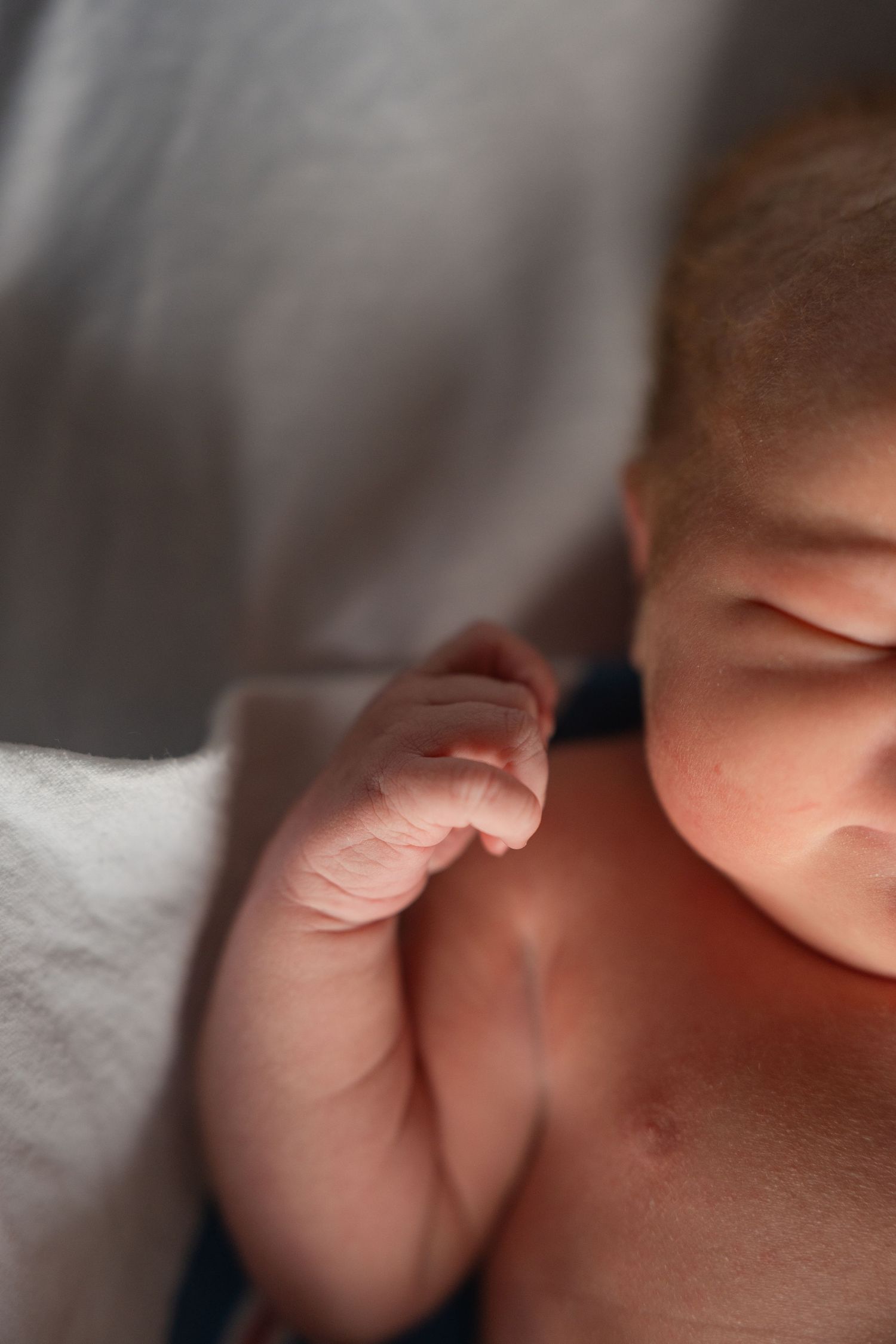 Close-up of a sleeping newborn baby's tiny hand and face in soft lighting.