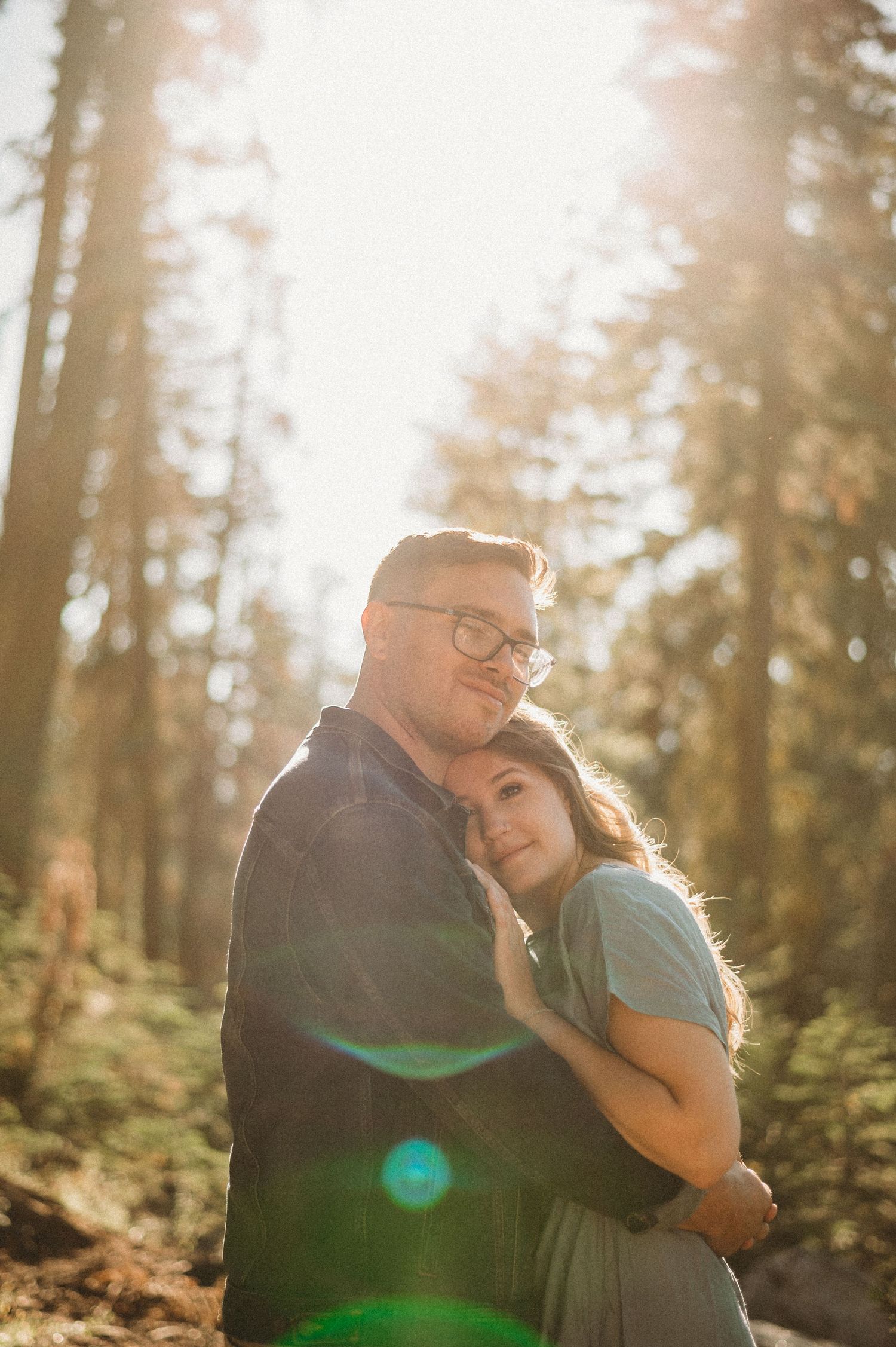 Couple embracing in sunlit forest, creating a romantic and intimate atmosphere.