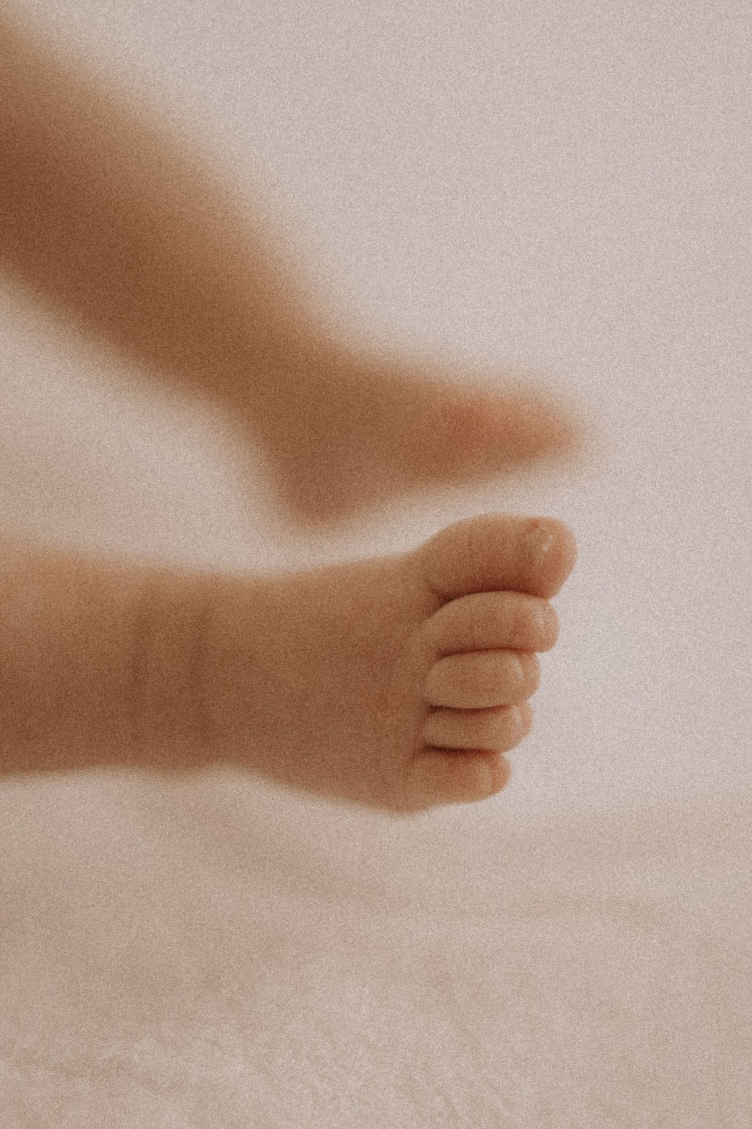 Close-up view of a tiny baby foot against a soft beige background in a gentle, dreamy style.