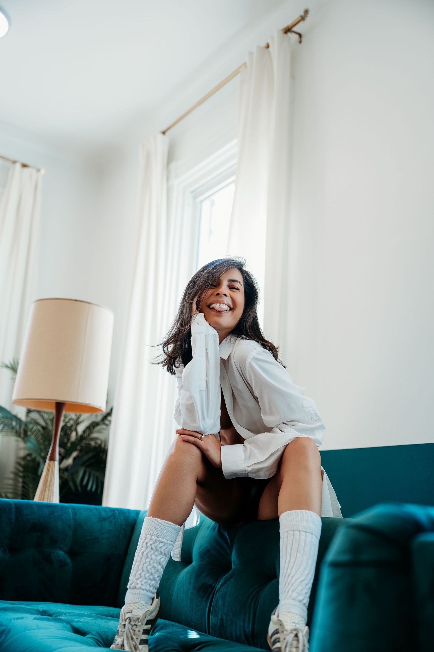 Person in white socks lounging on a teal velvet couch in a bright modern living room.