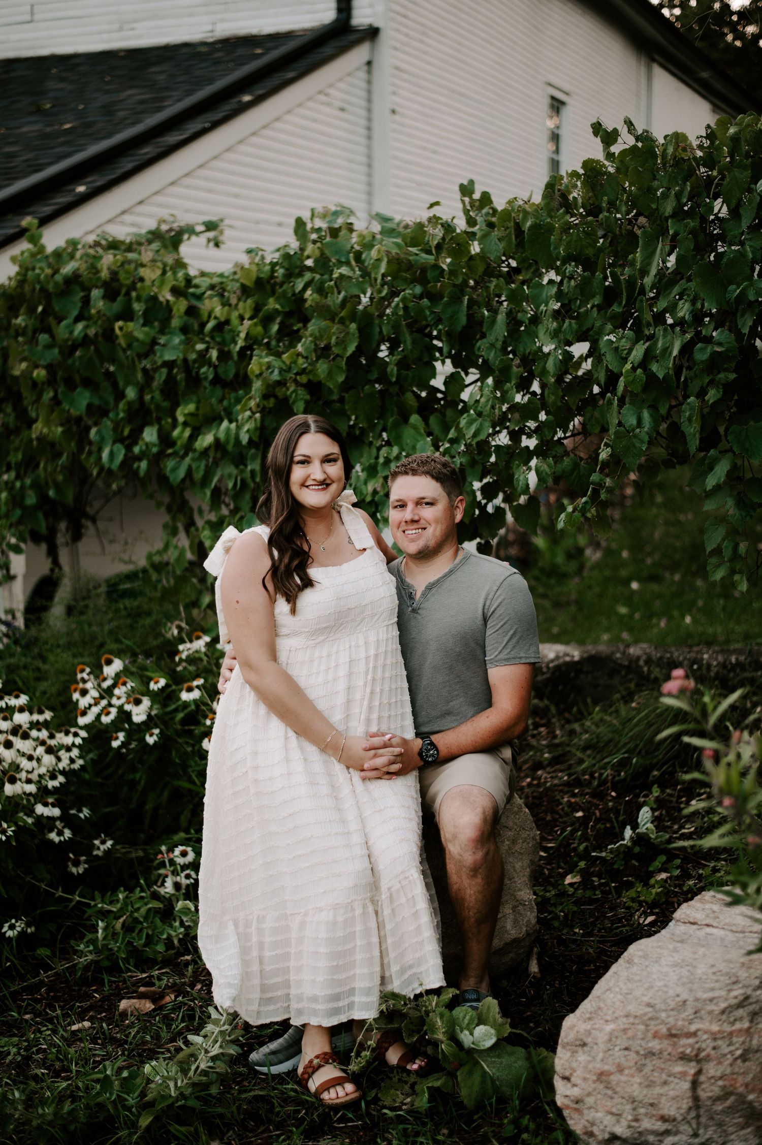 A couple shares a romantic moment together in a garden setting with lush green vines and white flowers in the background.