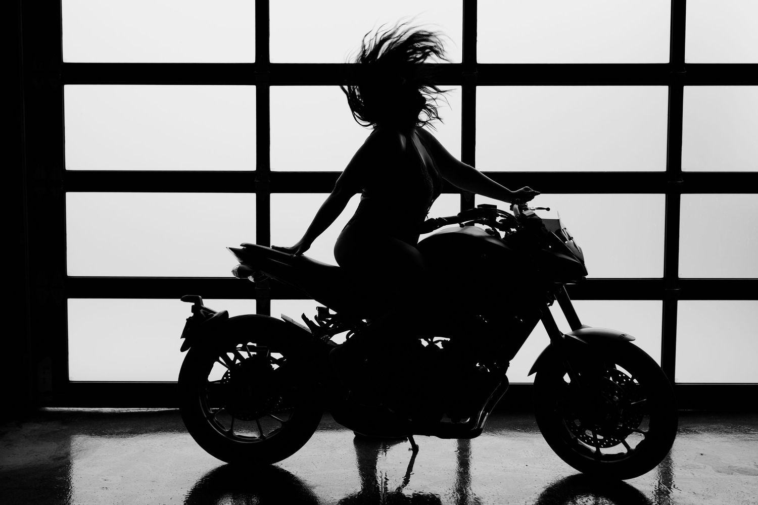 Sequence of silhouetted motorcycles shown against bright window panes creating a dramatic black and white composition.