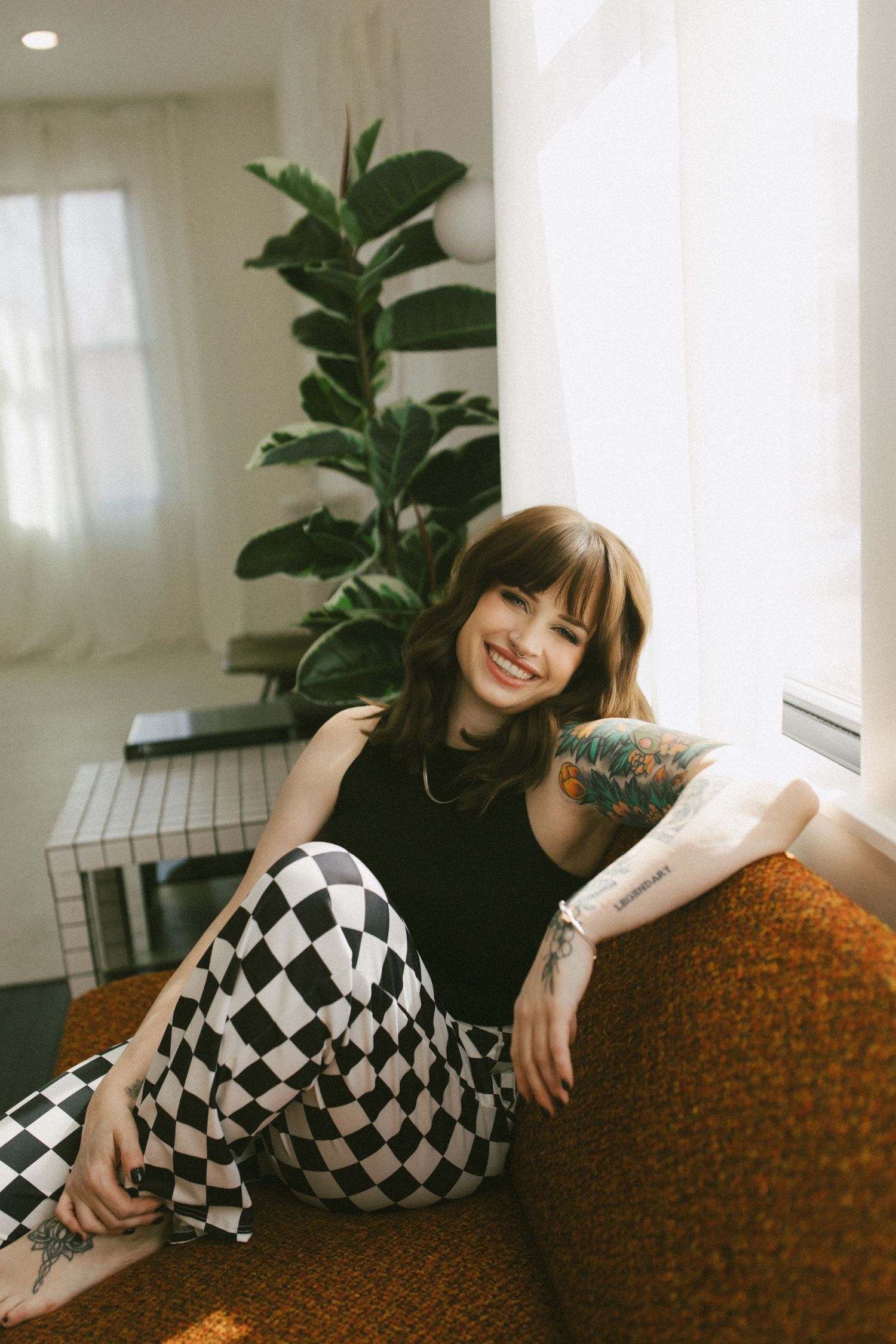 A person in black and white checkered pants lounges on a brown couch in a bright, modern interior space.
