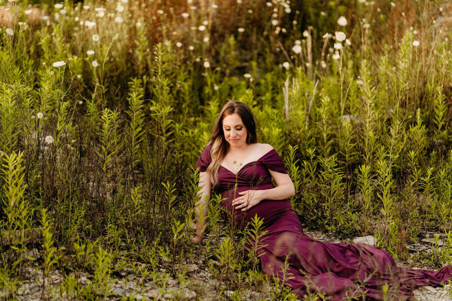 Woman in burgundy dress poses in a wildflower meadow during golden hour.