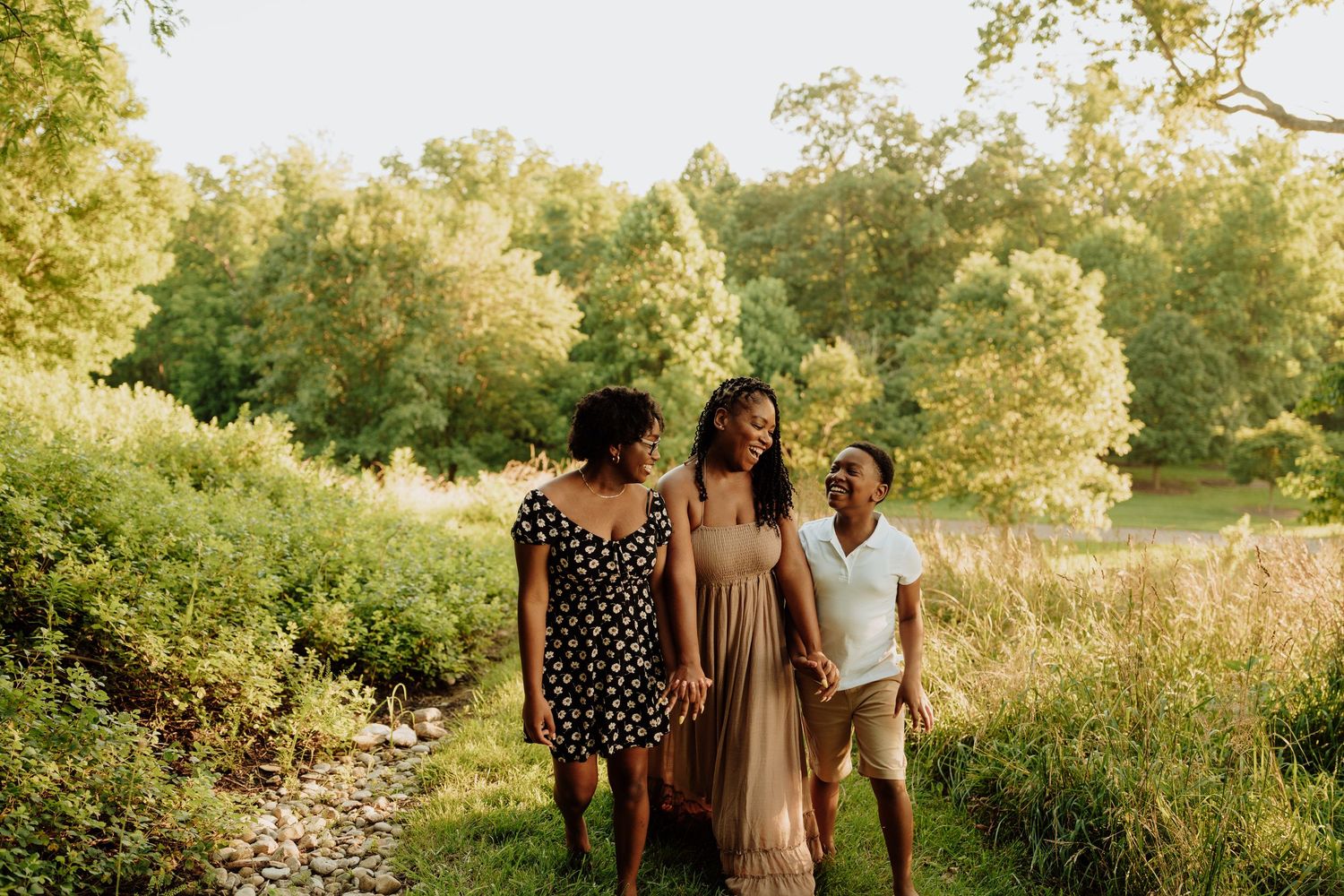 Three women walking together on a lush green nature path, smiling and enjoying a sunny outdoor stroll.