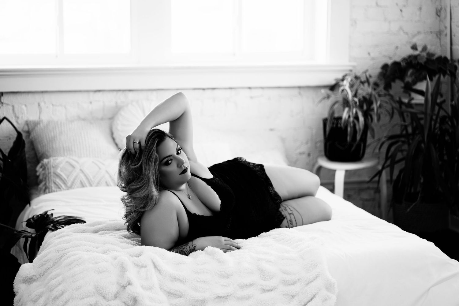 Black and white boudoir photography on bed with natural window lighting.