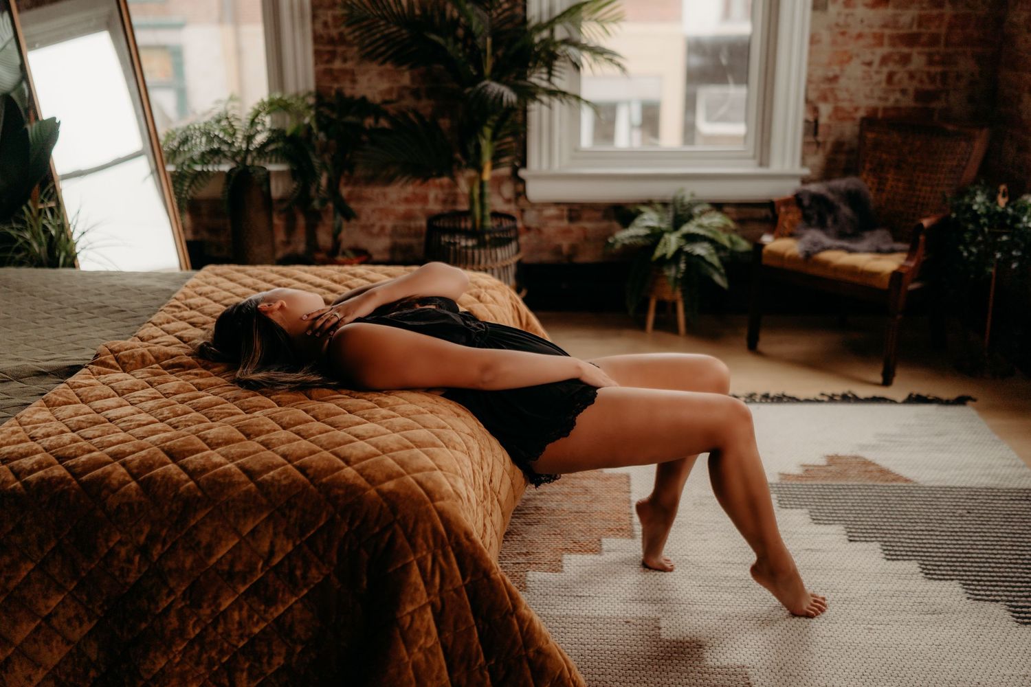 A person performs yoga stretches and poses on a wood floor in a sunlit room with brick walls and potted plants.