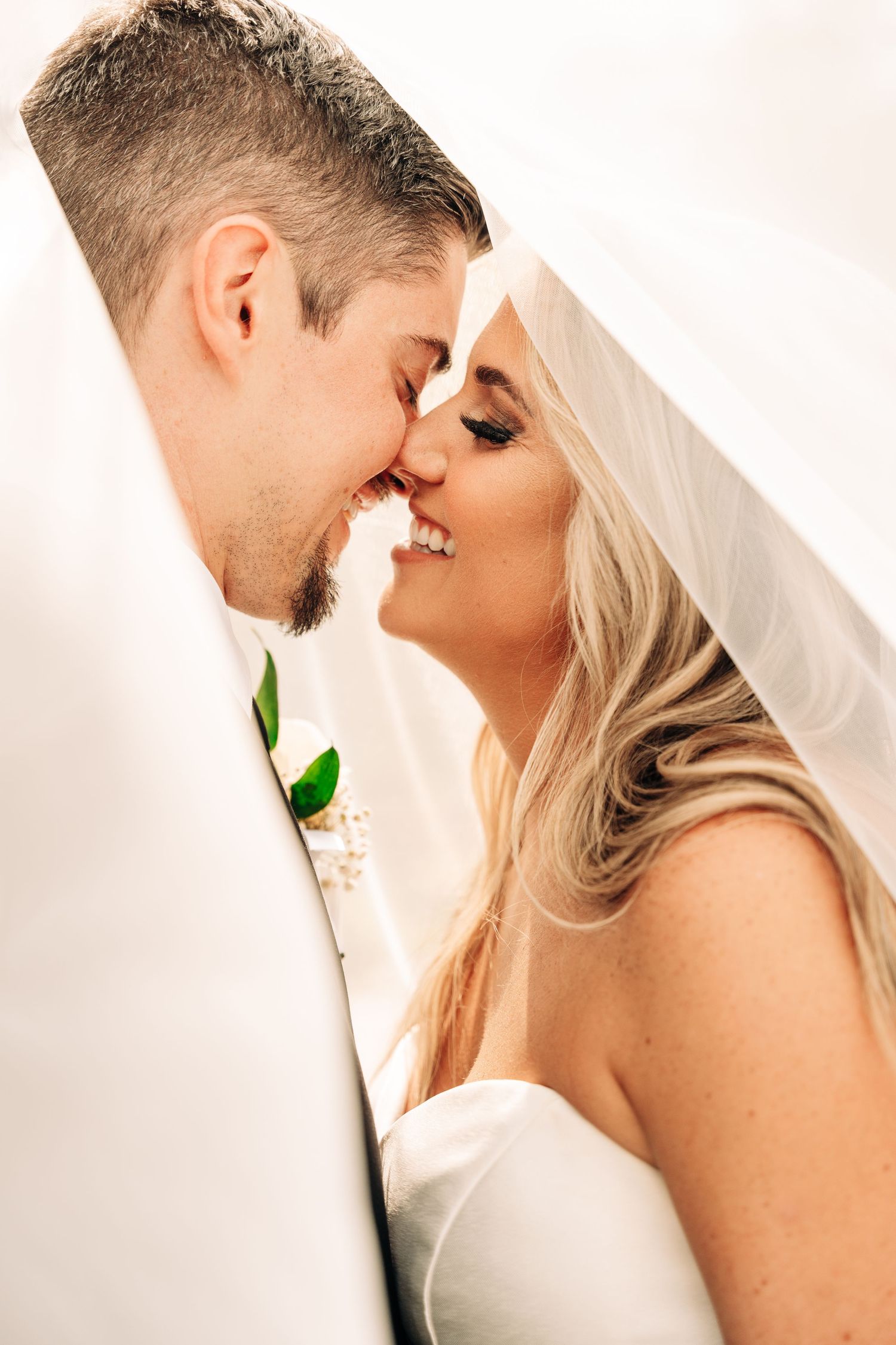 A romantic moment between newlyweds as they share an intimate close-up moment with the bride wearing a white veil.