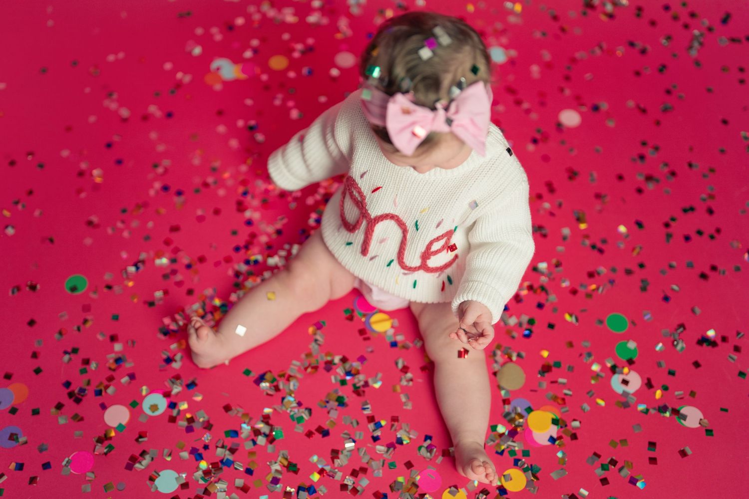 White ceramic baby shoes with confetti scattered on vibrant red background create a festive holiday scene.