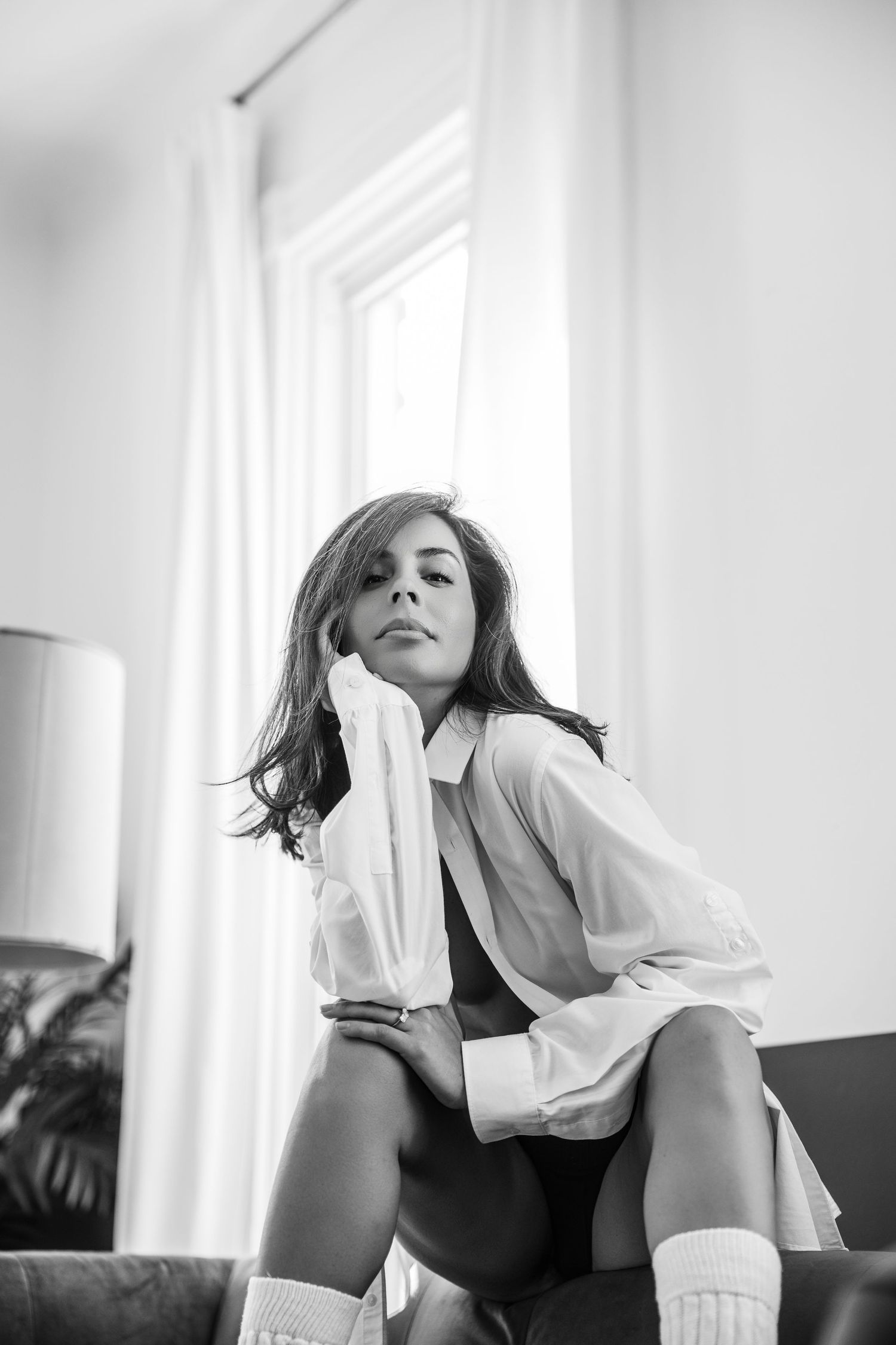 Black and white photo series showing a figure in white clothing reclining on a couch near bright windows.