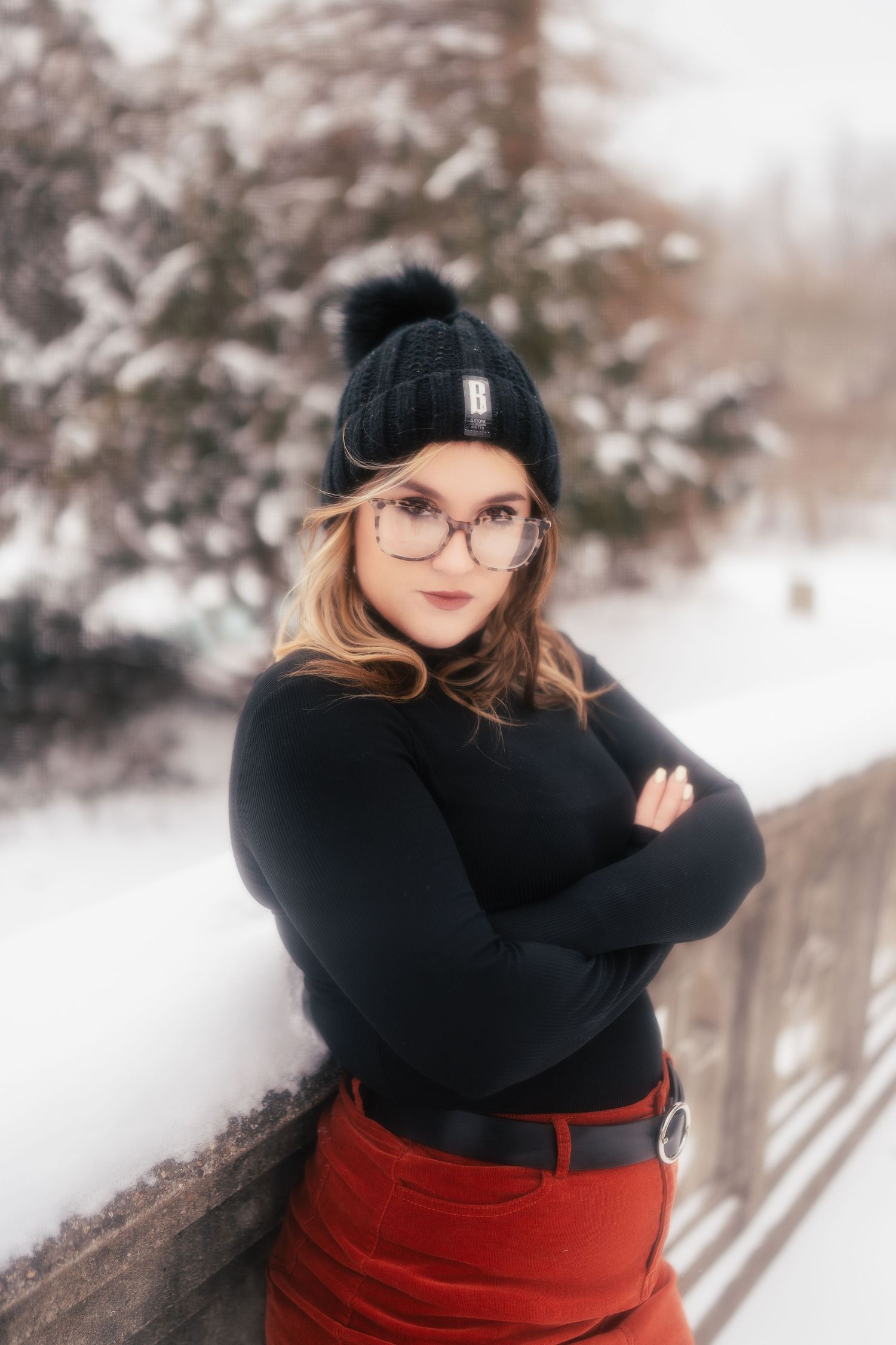 Winter fashion portrait with black beanie, glasses and sweater against snowy background with red skirt.