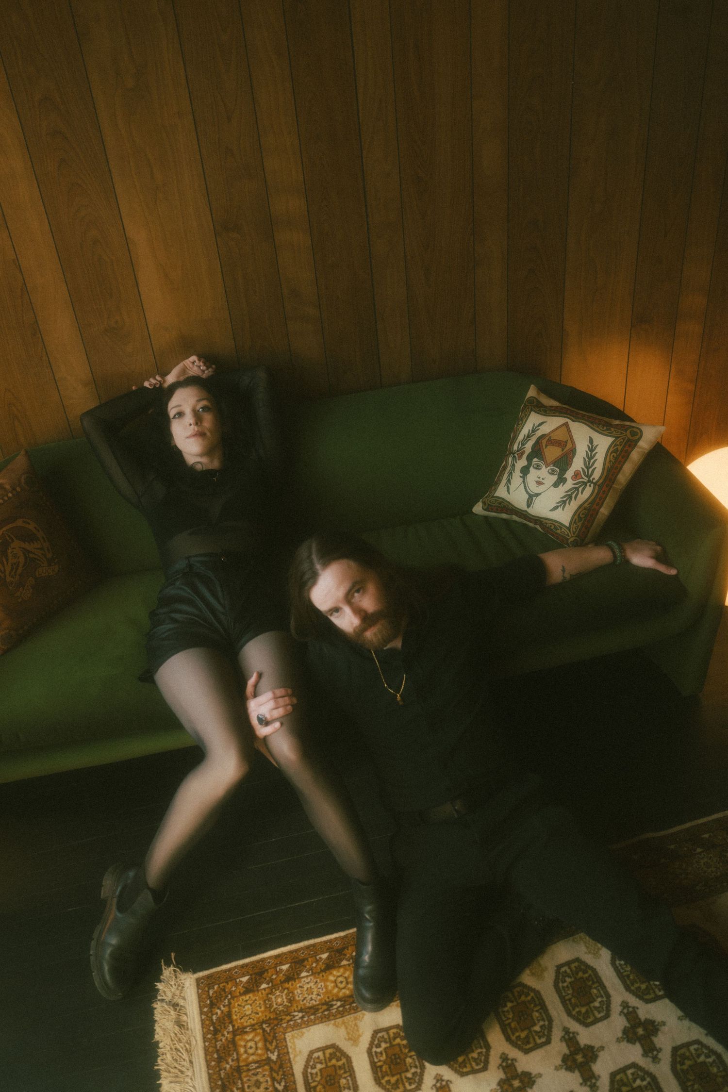 Person lying on dark green couch with decorative wooden box visible on floor in dimly lit room.