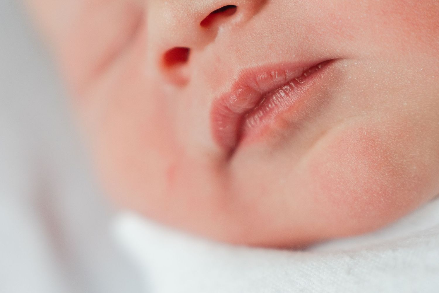 A tiny infant's mouth and nose up close against soft white fabric.