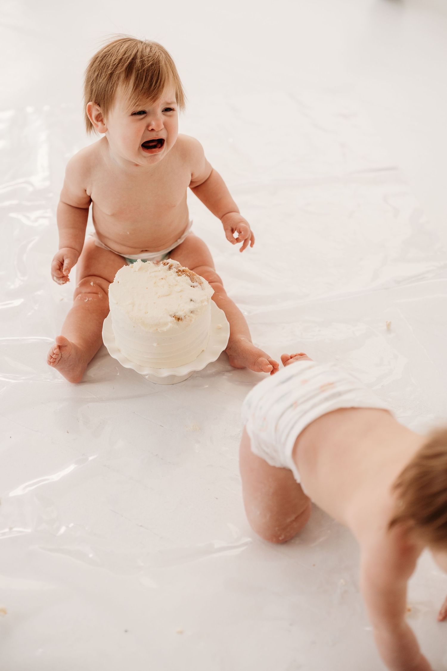 Baby wearing white diaper crawls and plays on white backdrop during photo session.