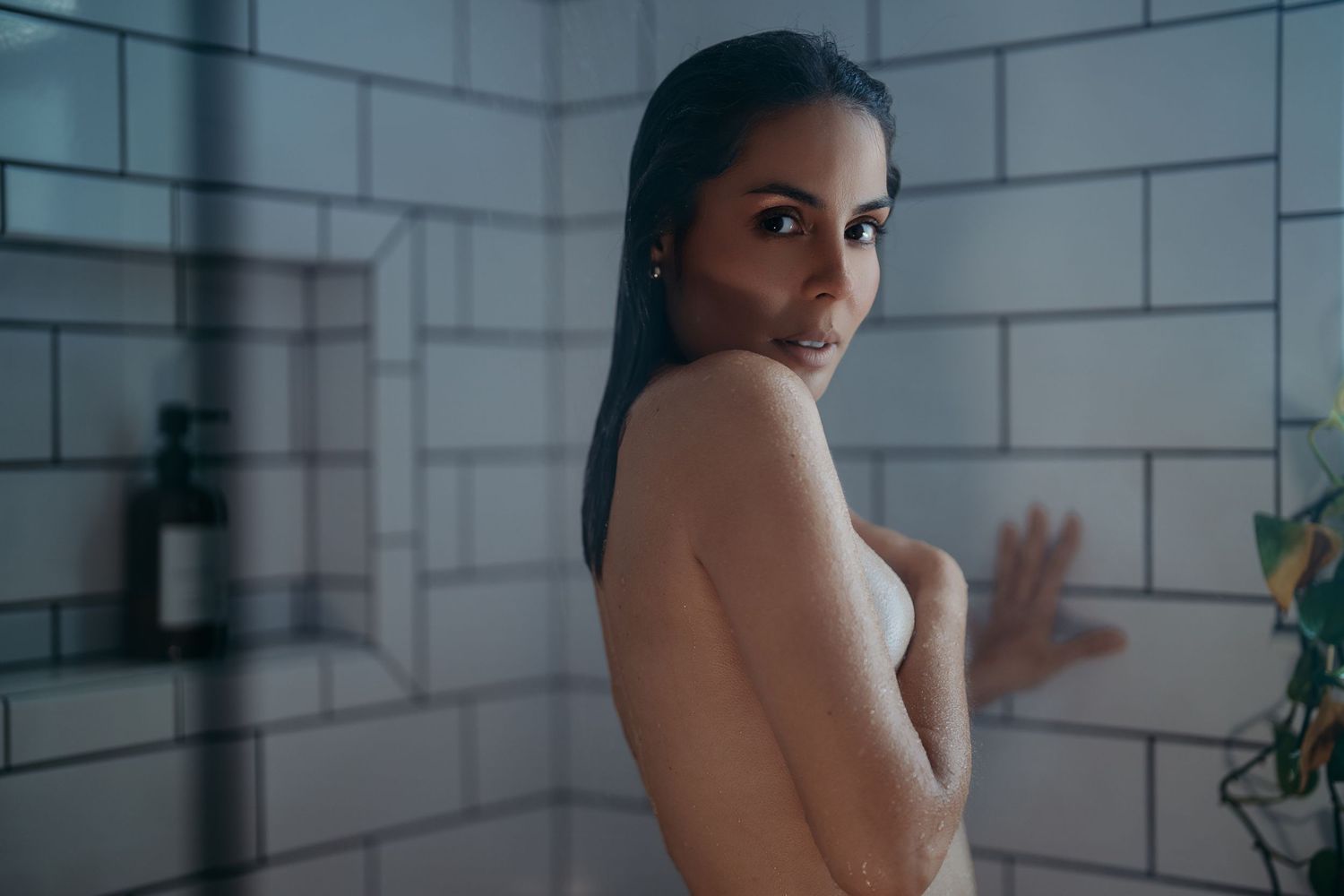 A moody portrait in a bathroom with white subway tile walls and dramatic lighting.