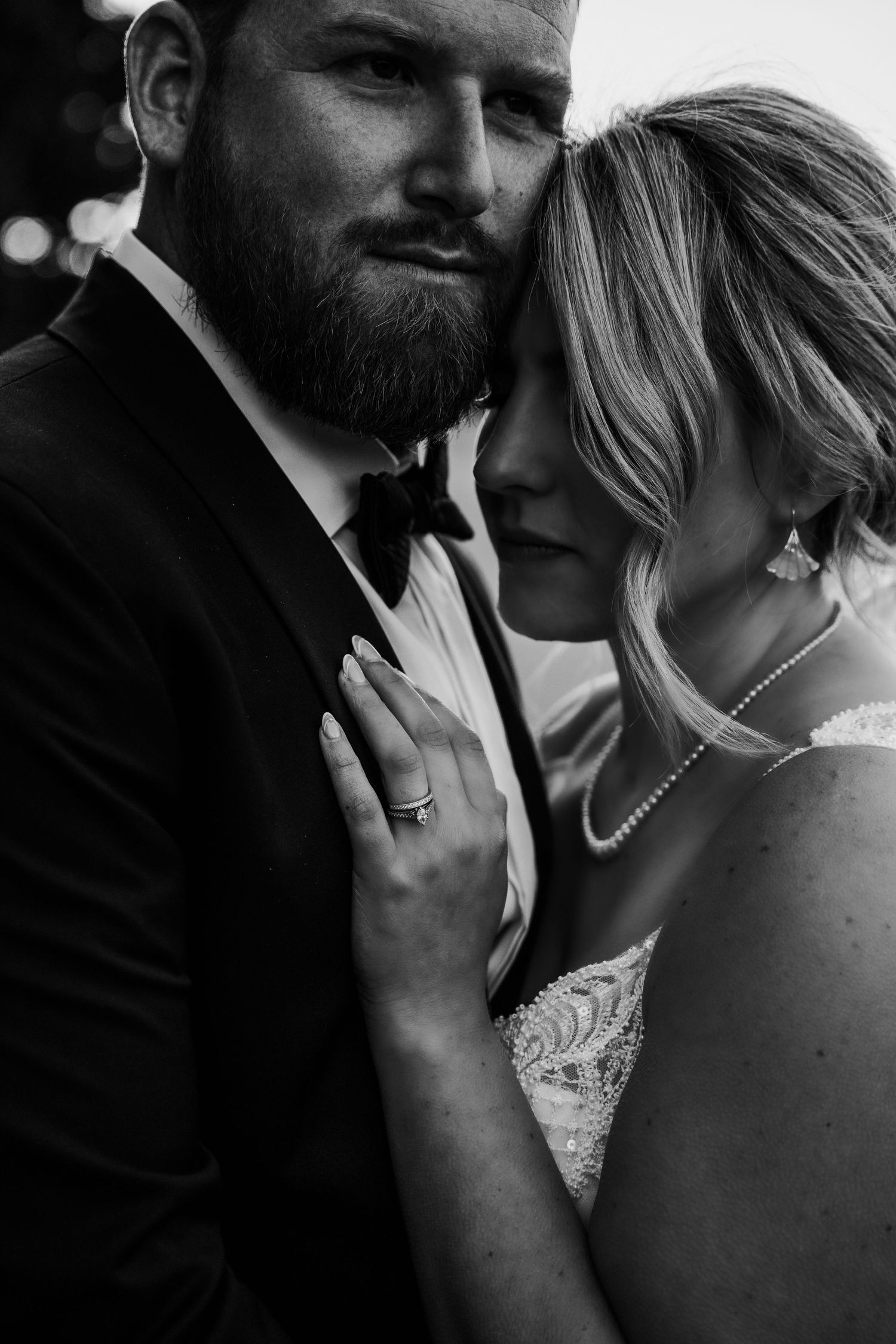 A black and white close-up of a couple embracing, with the man in a suit and the woman in a white dress.