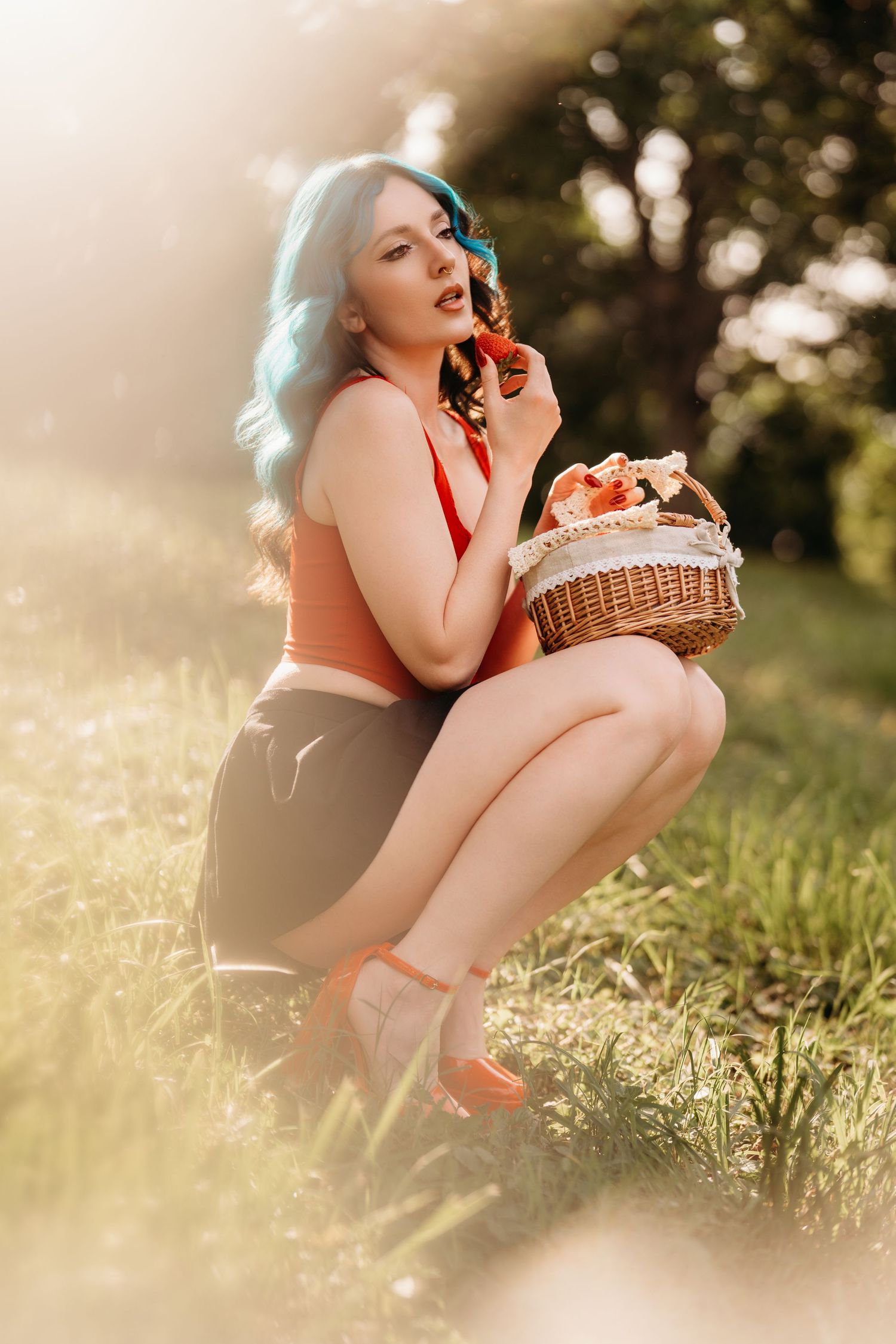 A woman with blue hair in a retro pin-up style sits outdoors holding a wicker basket in warm sunlight.