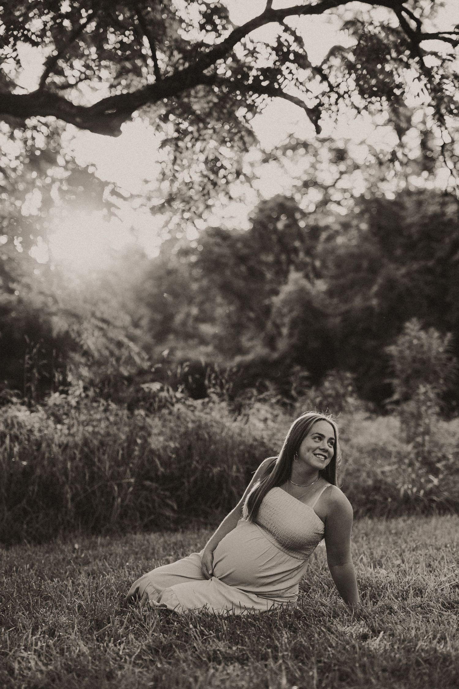 Black and white portrait series of a person laying in grass with natural sunlight filtering through trees.