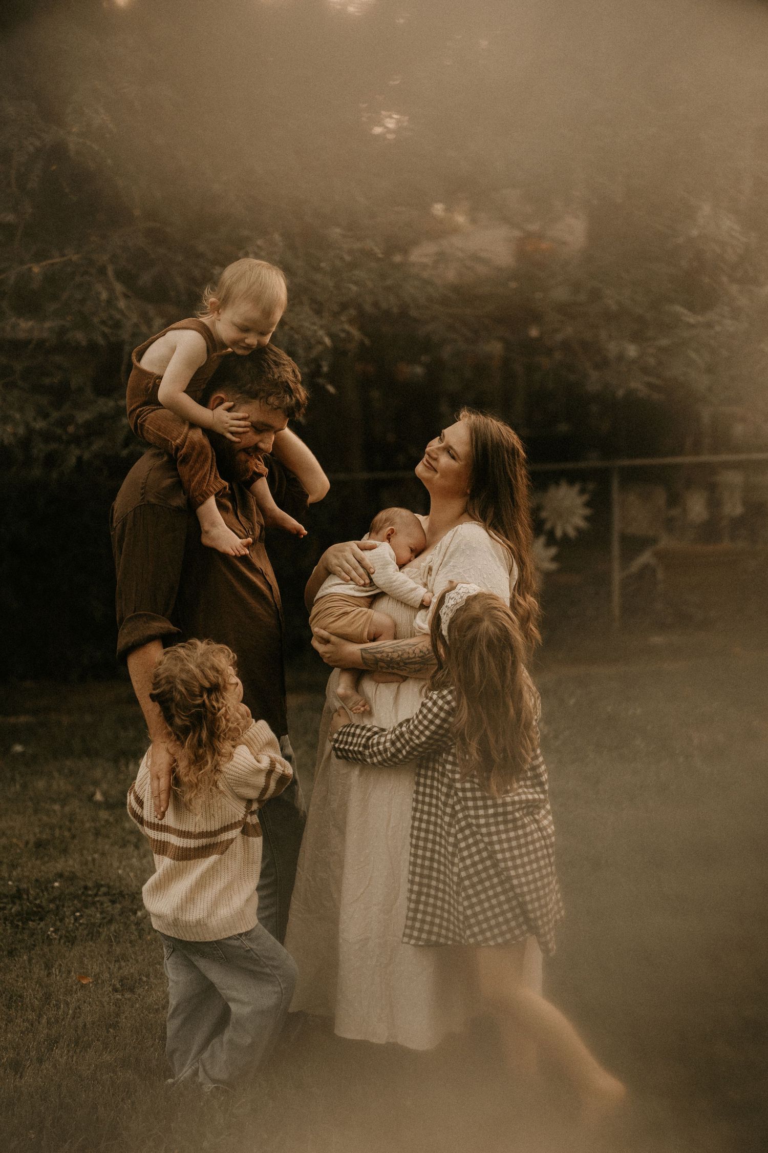 A joyful family of five laughs together outdoors, with parents holding young children in a warm, candid moment.