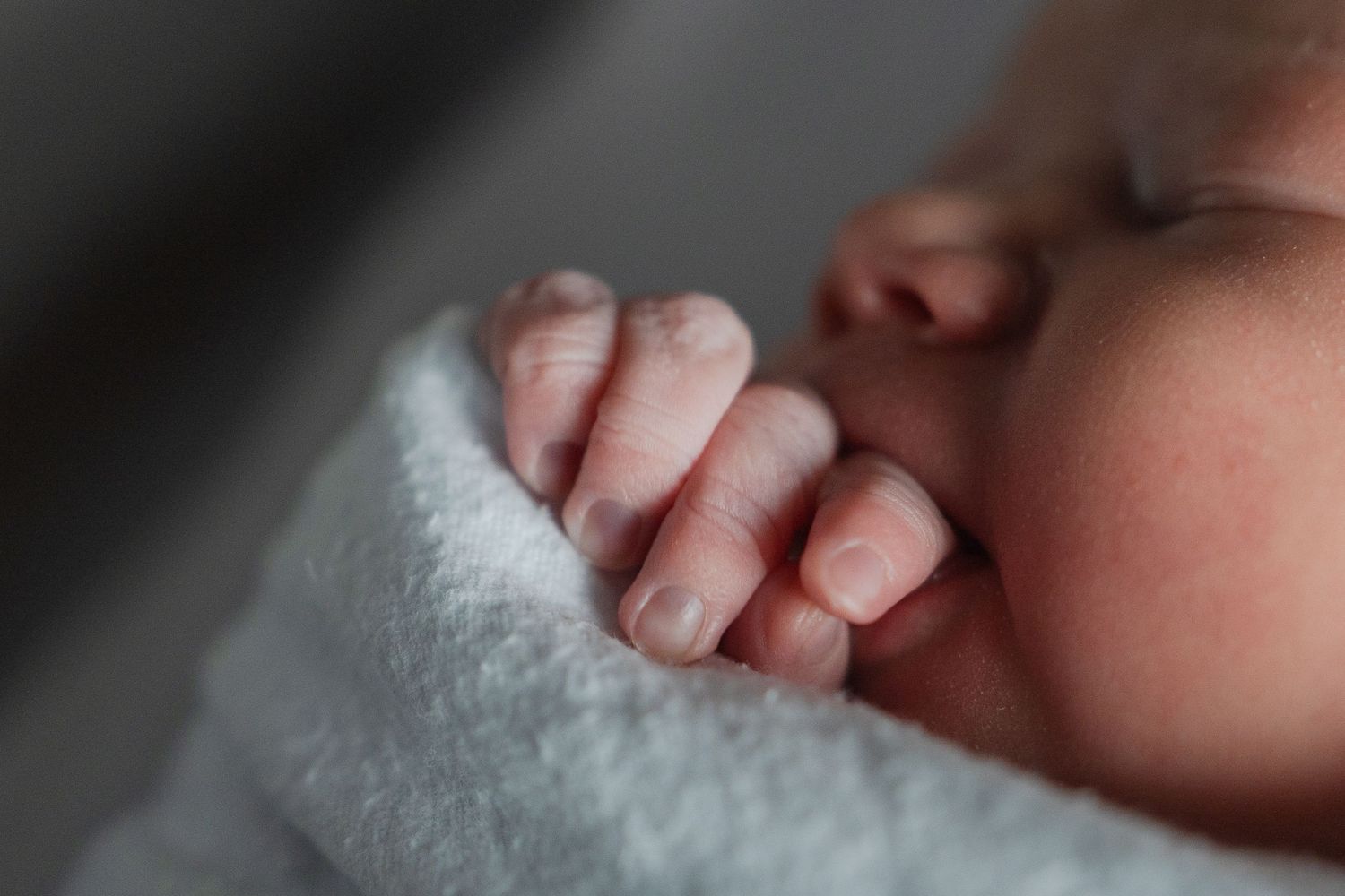 Close-up photo of a tiny baby's hand wrapped in a soft white blanket.