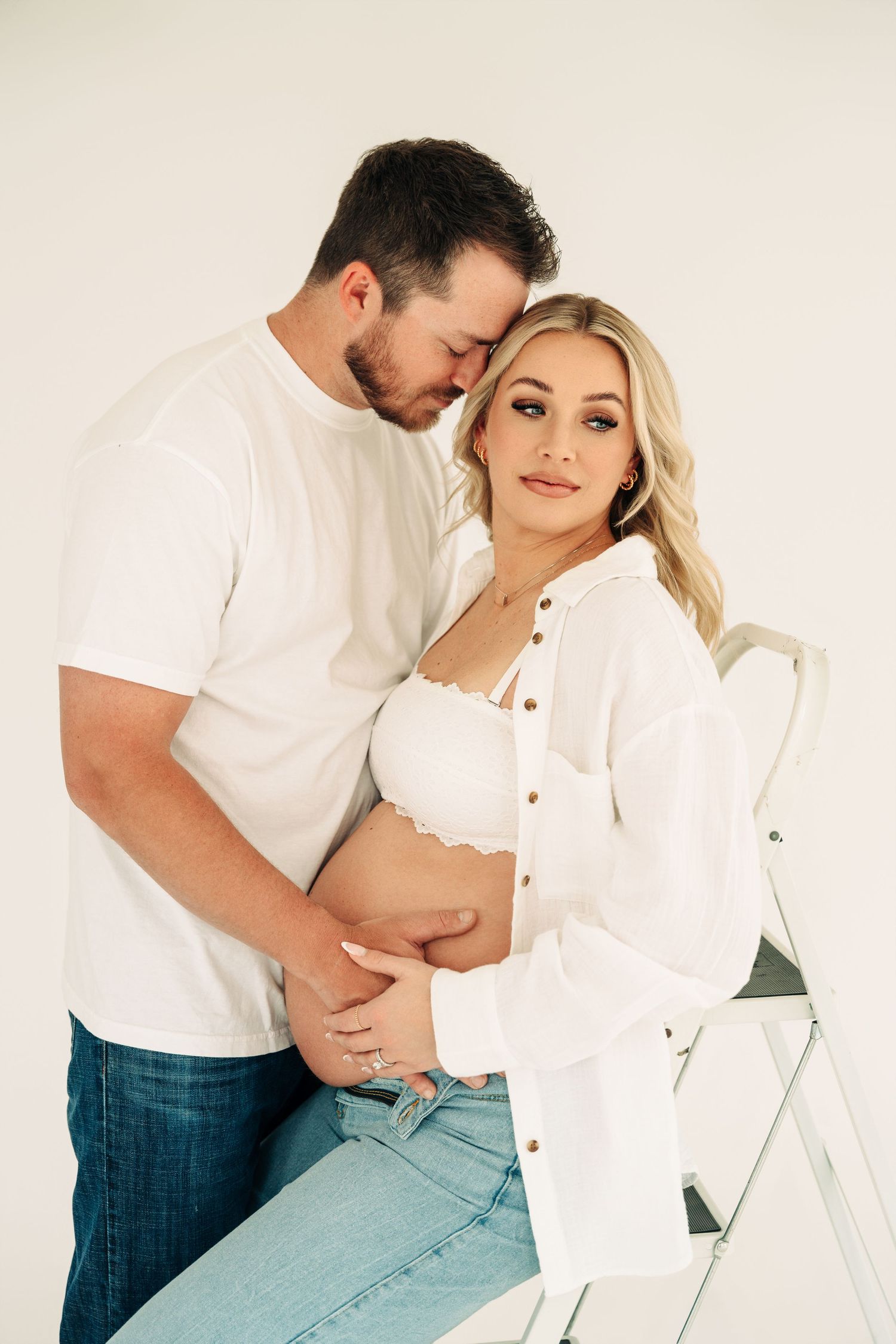 A romantic couple in white and denim poses intimately against a light backdrop in a series of tender moments.