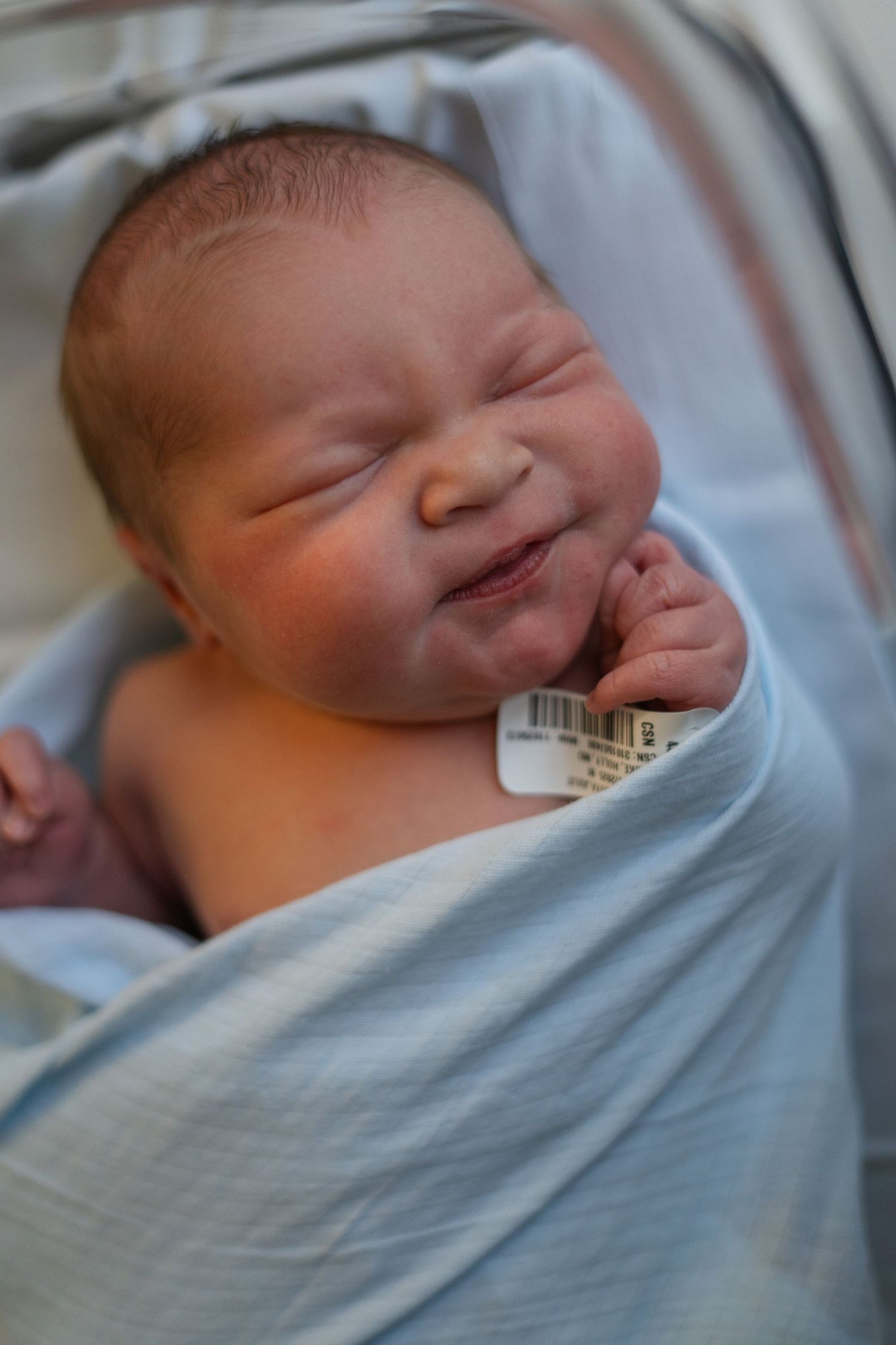Smiling newborn baby swaddled in light blue blanket resting peacefully.