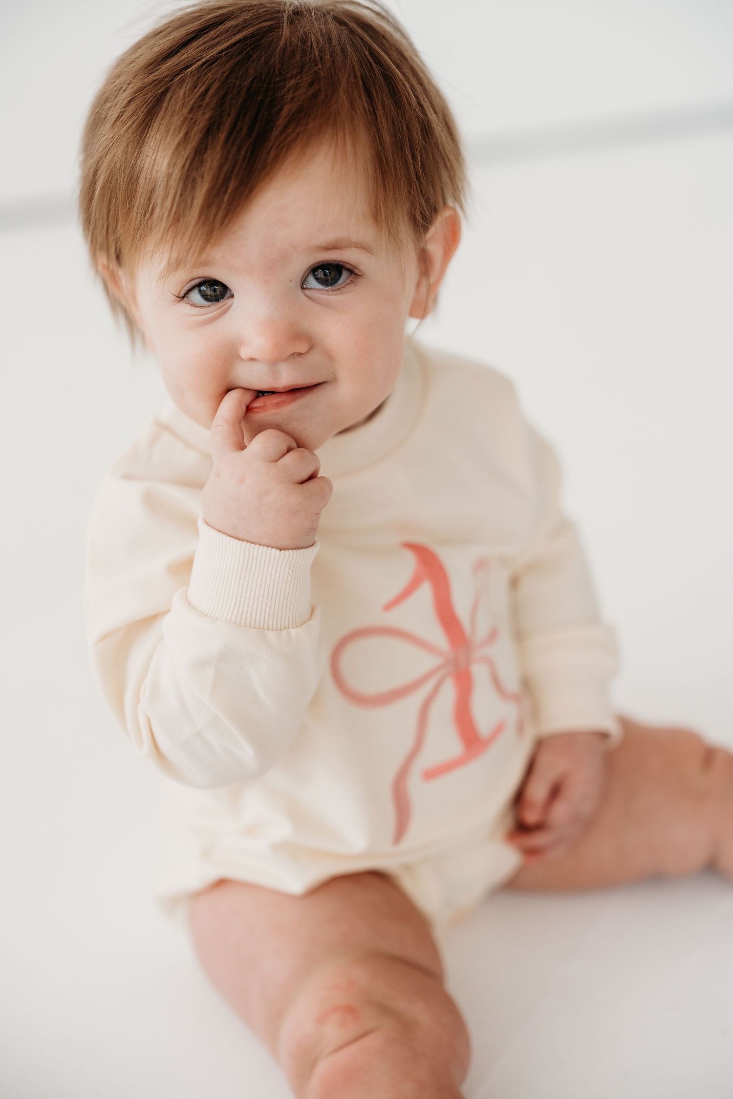Sweet baby in cream-colored sweater lying on white background showing playful expressions in four candid poses.