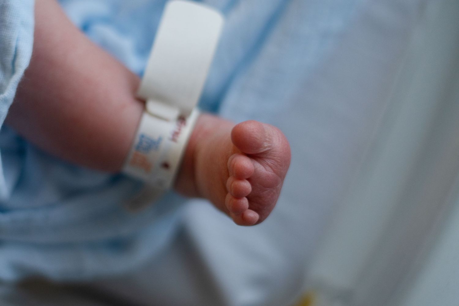 Close up detail shot of a newborn baby's tiny foot with hospital ID bracelet against blue background.