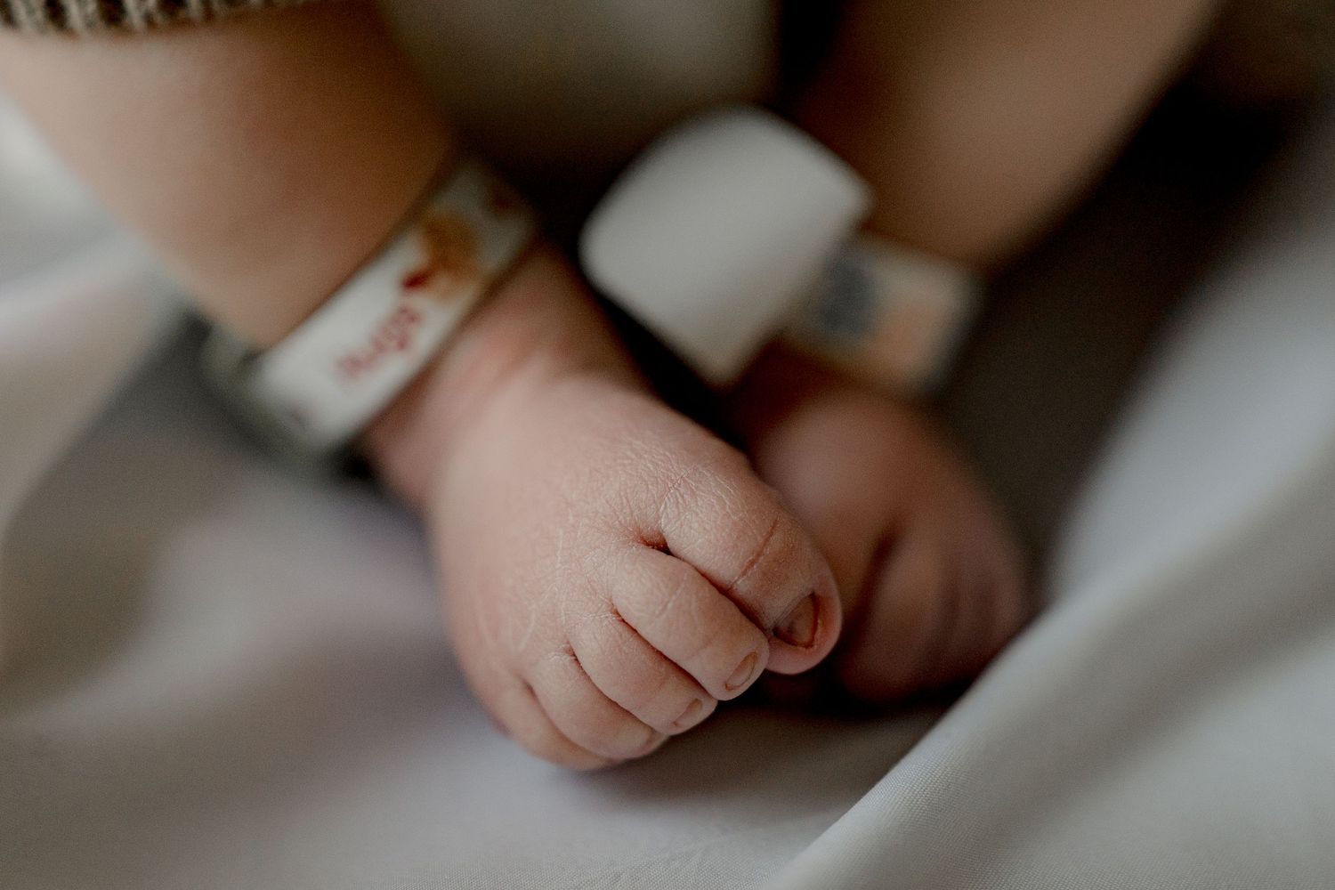 Close-up view of baby hands and feet on soft white bedding showing delicate details and textures.
