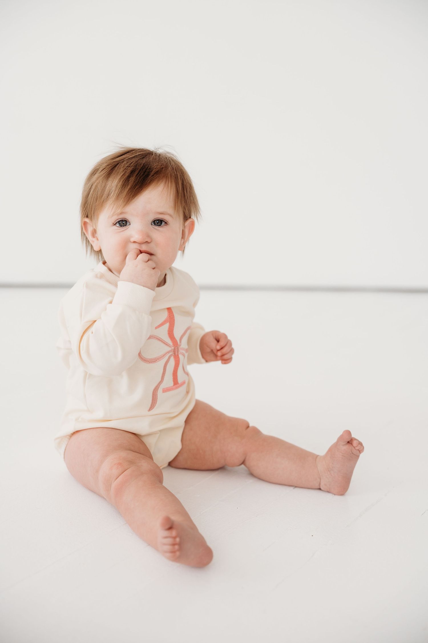 A baby in a white onesie sits and crawls on a white backdrop in a series of lifestyle photography poses.
