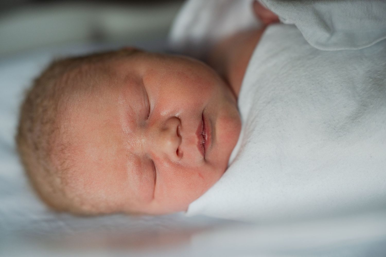 Peaceful newborn resting on soft white blankets in gentle lighting.