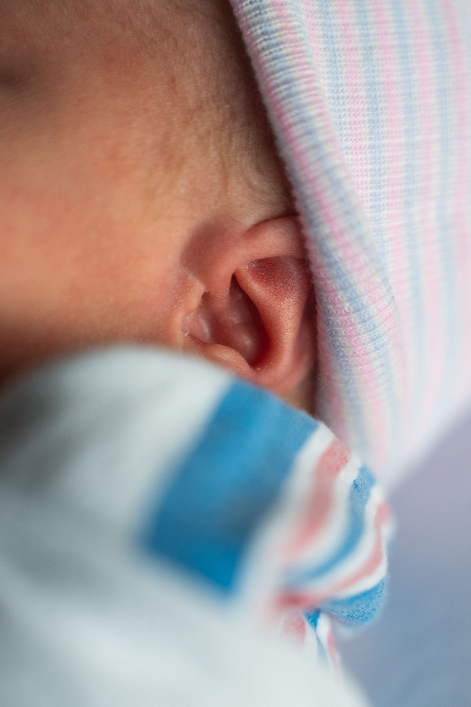 Close-up view of a sleeping newborn baby wearing a pink and blue striped hat.