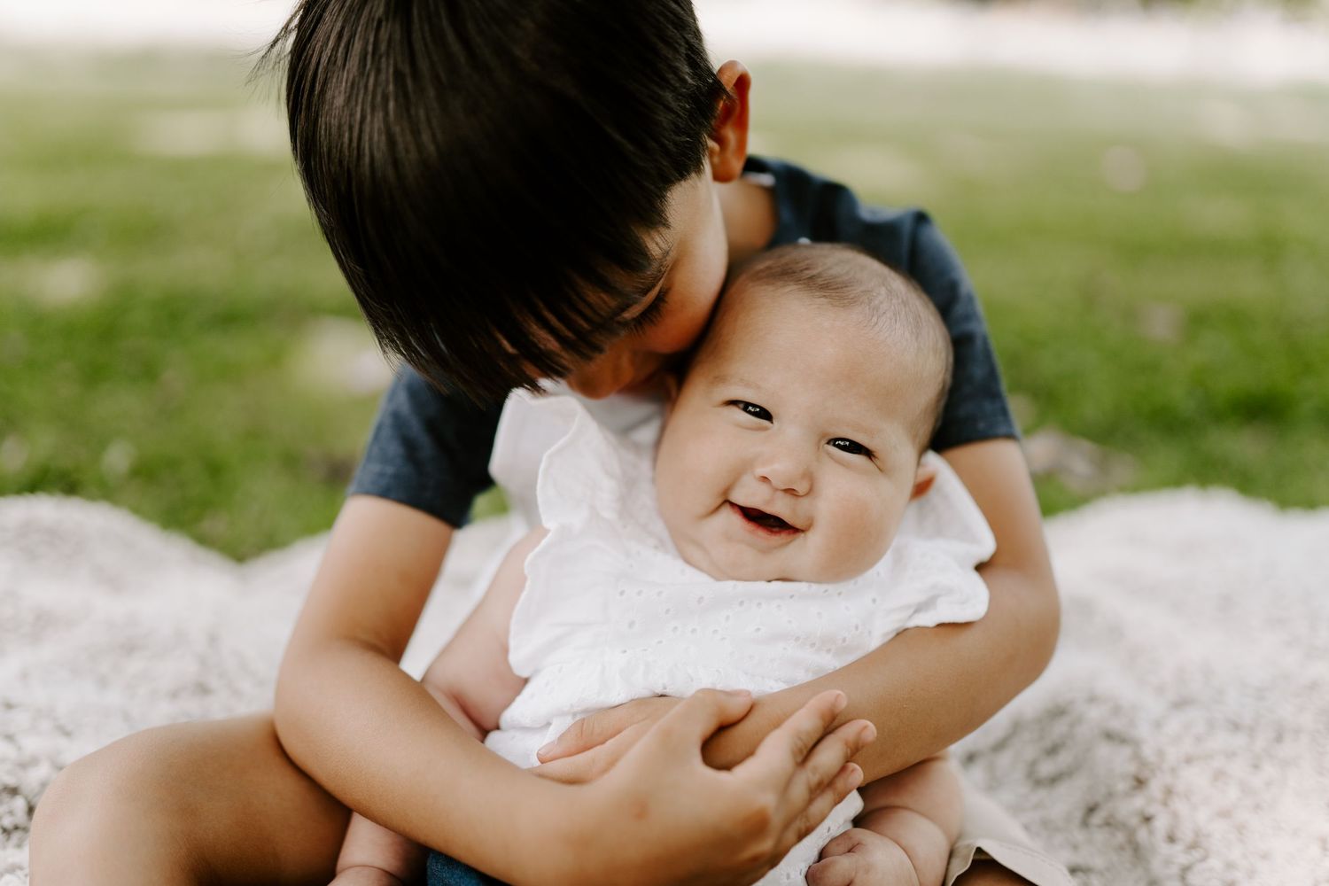 A tender moment captured outdoors on a blanket shows siblings sharing a heartwarming interaction and joyful laughter.