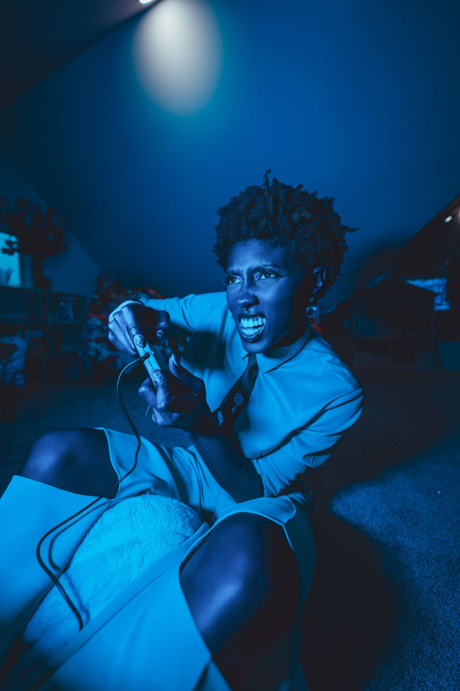 A performer in a white outfit sings passionately into a microphone against a deep blue-lit background.