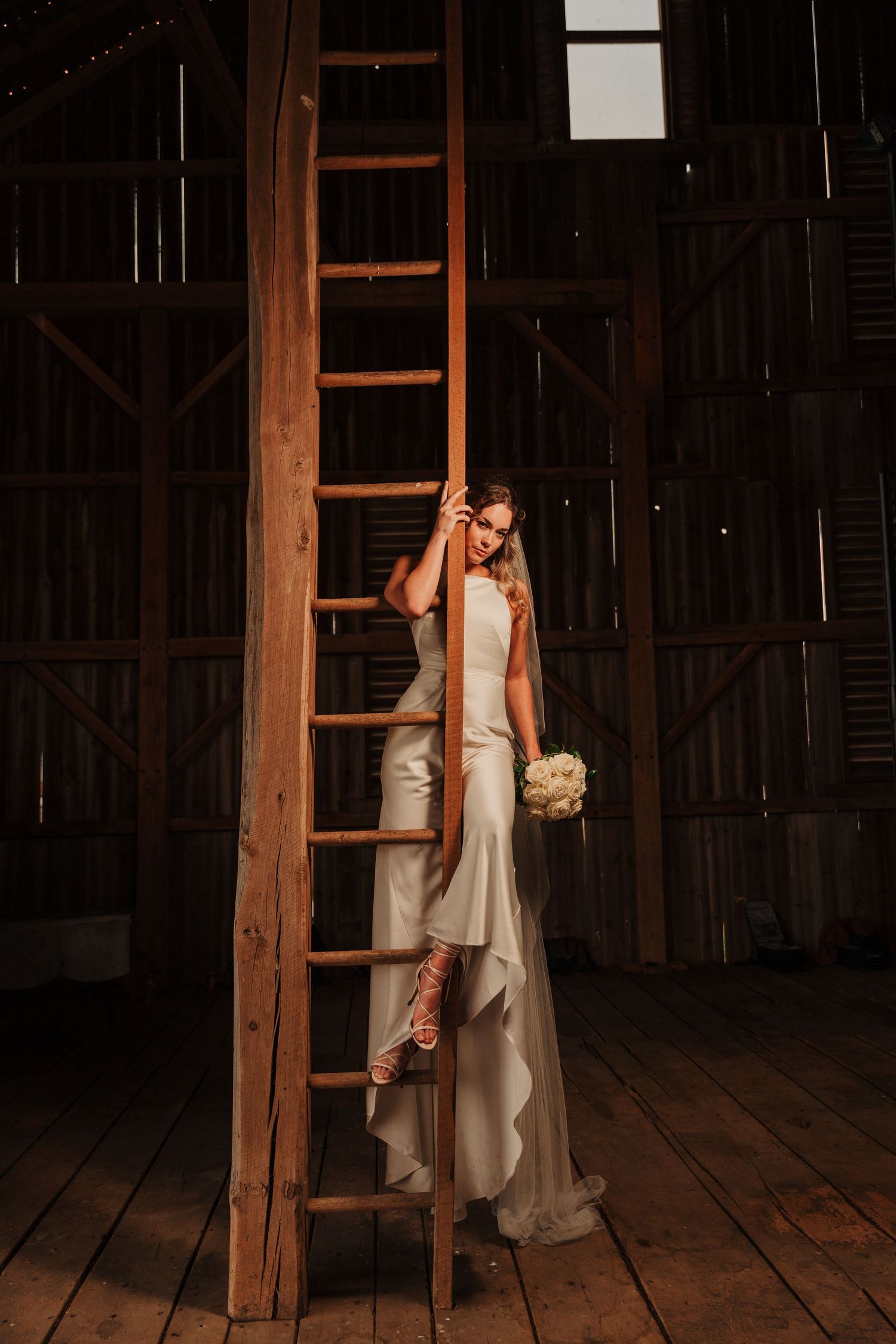 Romantic wedding couple shares intimate moments in a rustic wooden barn with dramatic lighting and shadows.