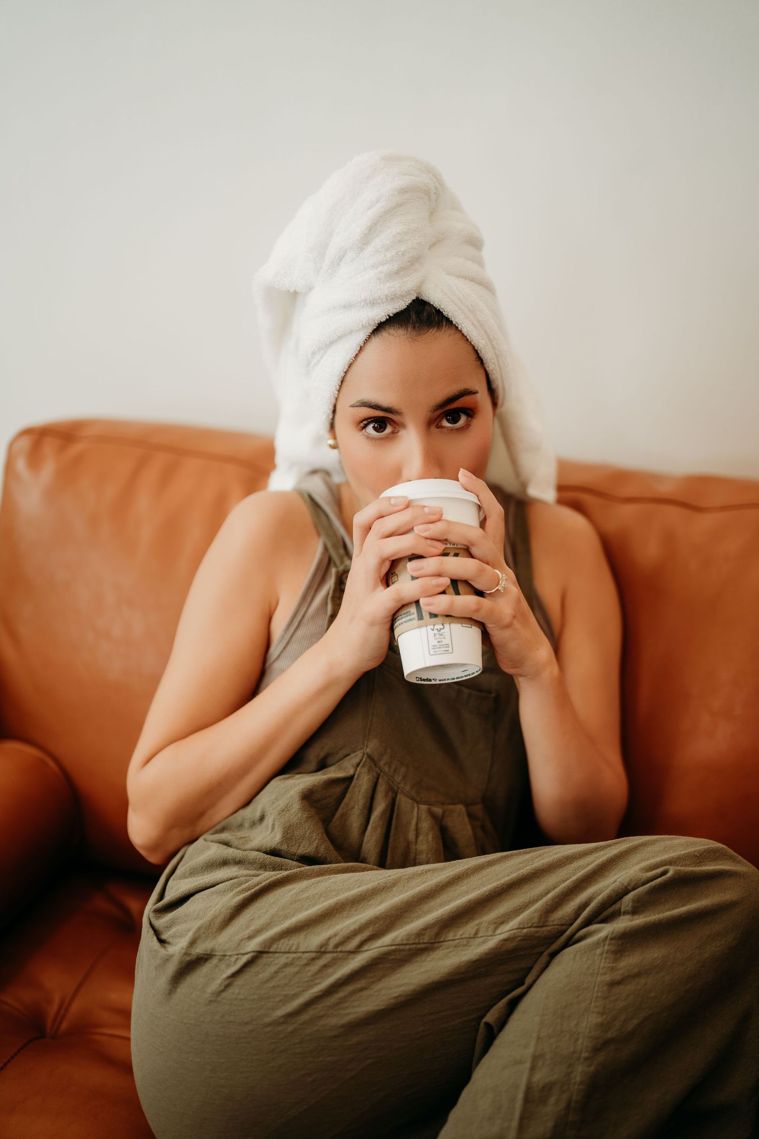 Person in olive green dress lying on brown leather couch while drinking from white mug in progressive photo sequence.