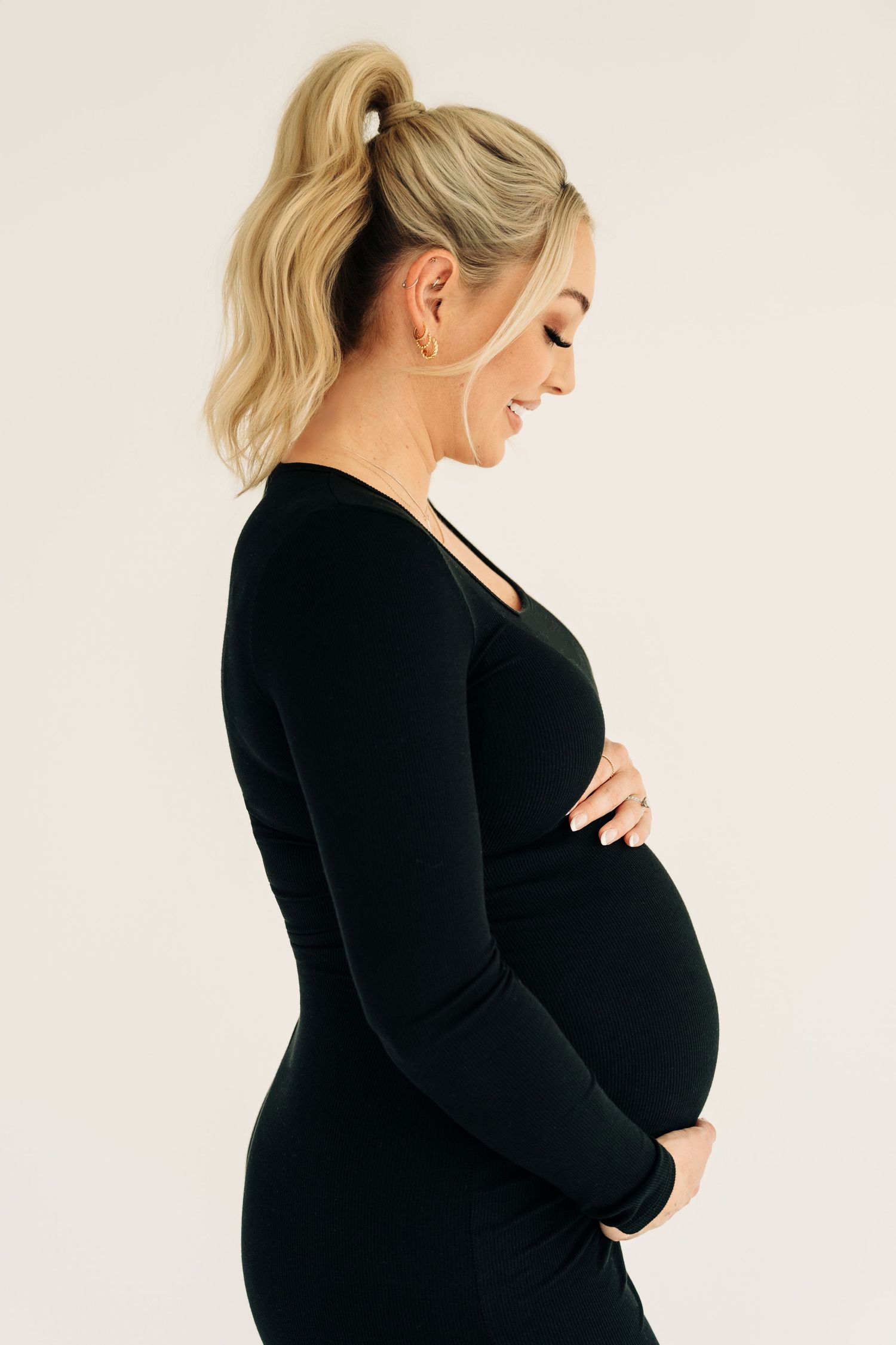 A pregnant woman in a black long sleeve dress poses in a series of side profile shots against a white background.