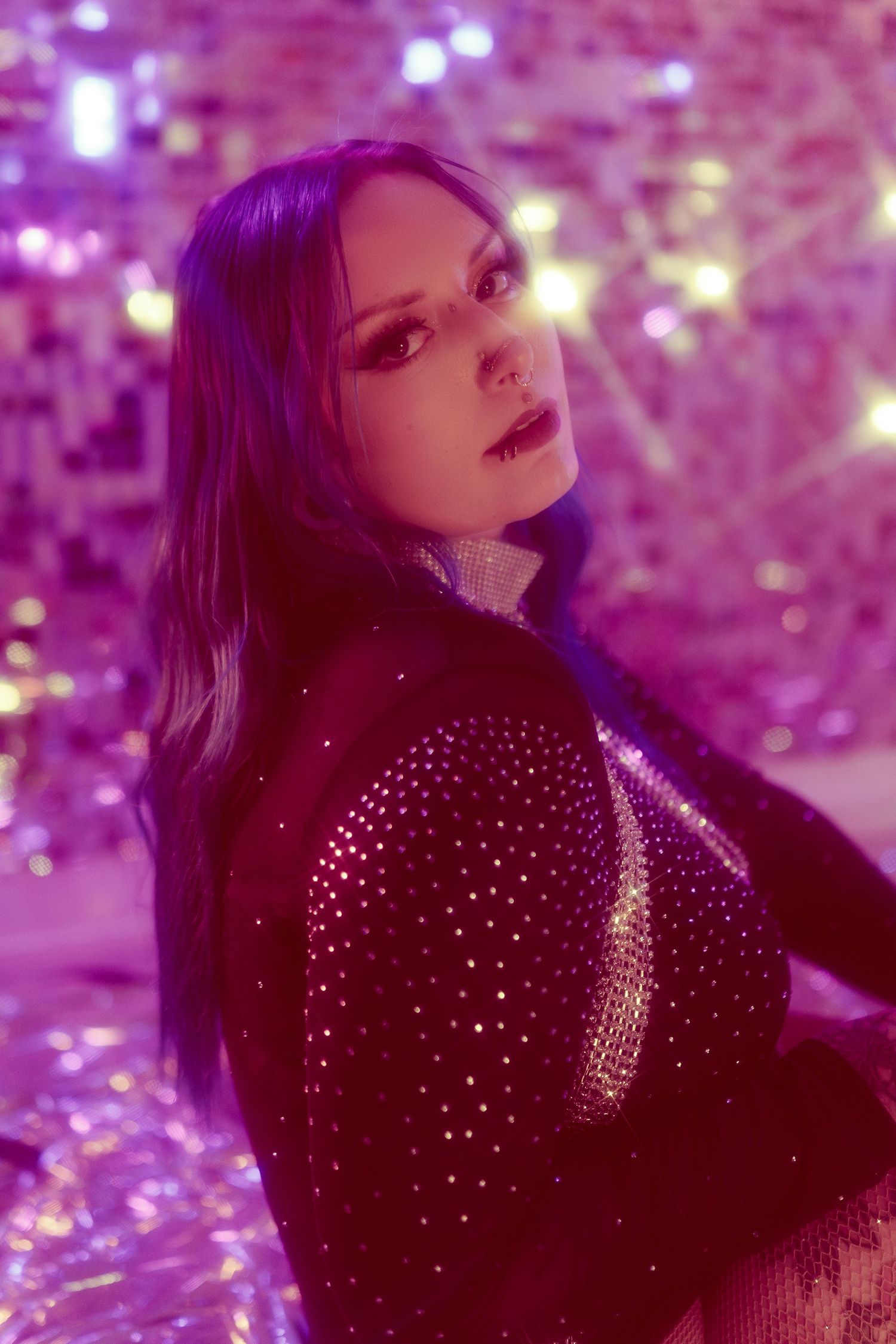 A figure poses in a sparkly black dress against a purple-lit background with bokeh effects creating a dreamy atmosphere.