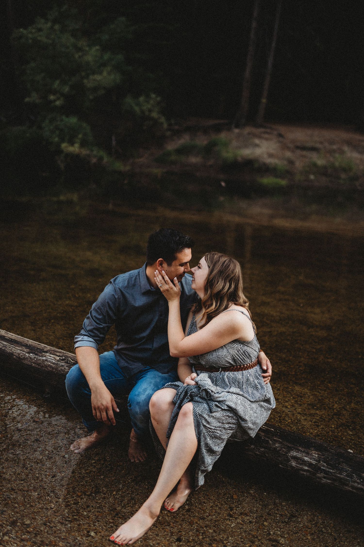 Couple sitting on log by water, sharing an intimate moment in nature.