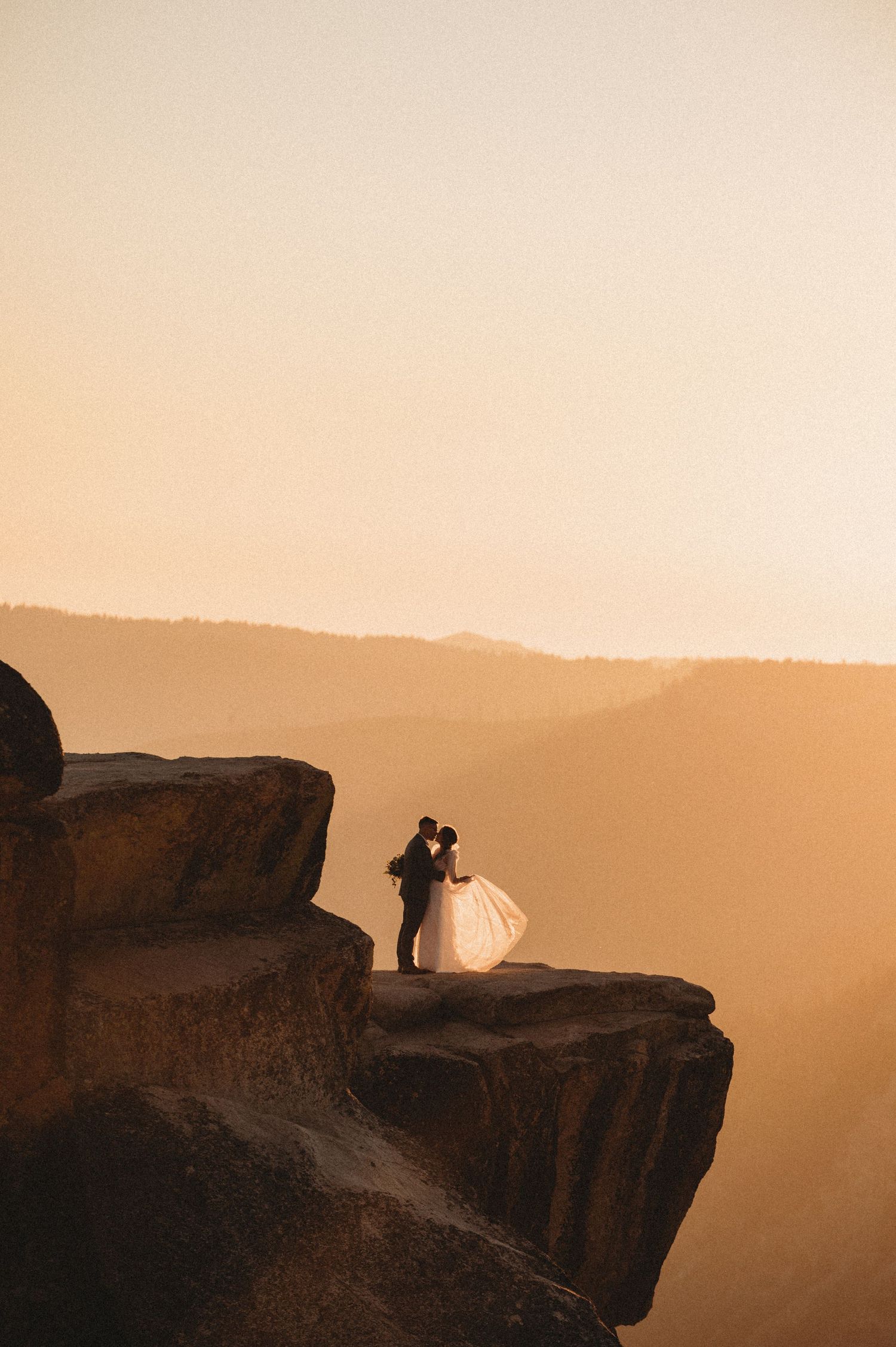 Silhouetted figures stand on a dramatic cliff edge against a misty golden sunset in Yosemite National Park.