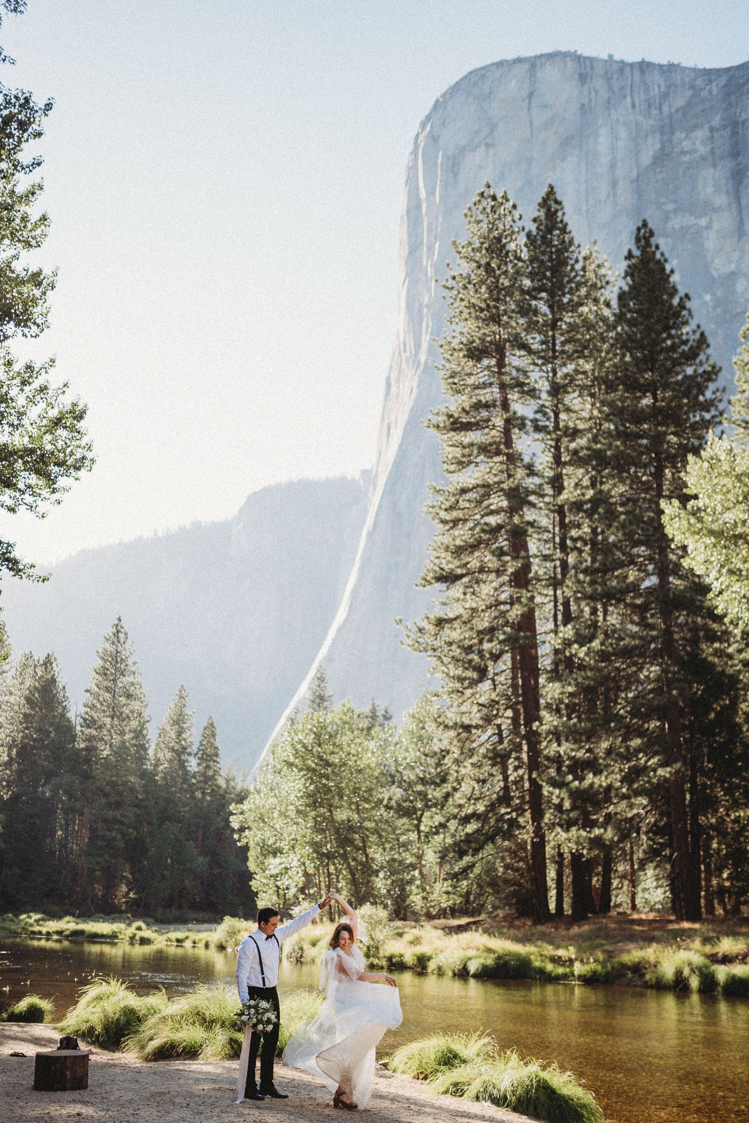 Wedding couple poses in a scenic meadow with El Capitan's granite face towering in Yosemite Valley.