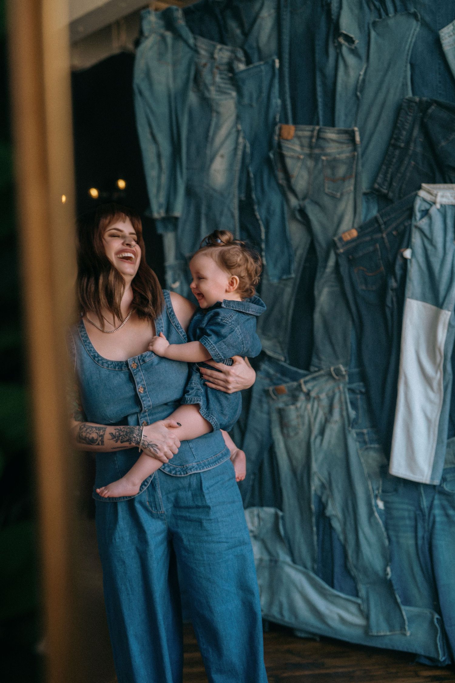 Mother and child share tender moments against wall of hanging denim jeans in artful photo series.