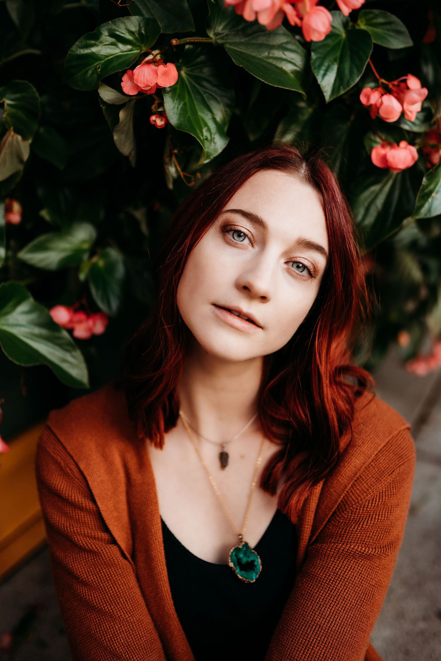 Portrait series against coral flowers and green foliage showing different angles in a rust-colored sweater and black top.
