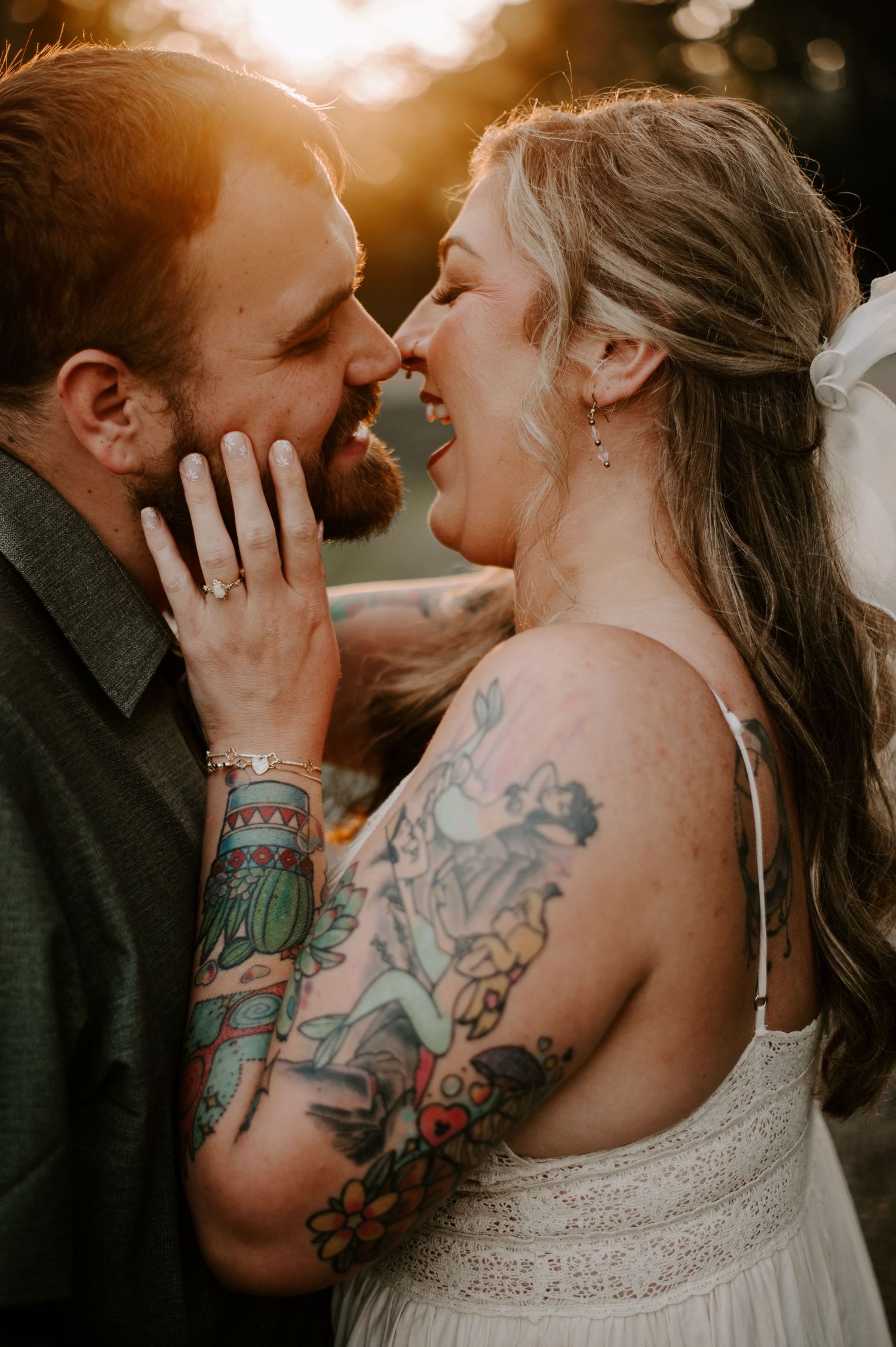 A couple in a romantic embrace, with the woman's colorful arm tattoos visible against her white dress.