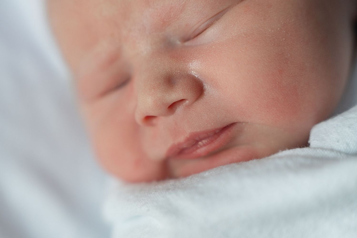 Gentle profile shot of a peaceful sleeping infant wrapped in white and pink striped fabric.